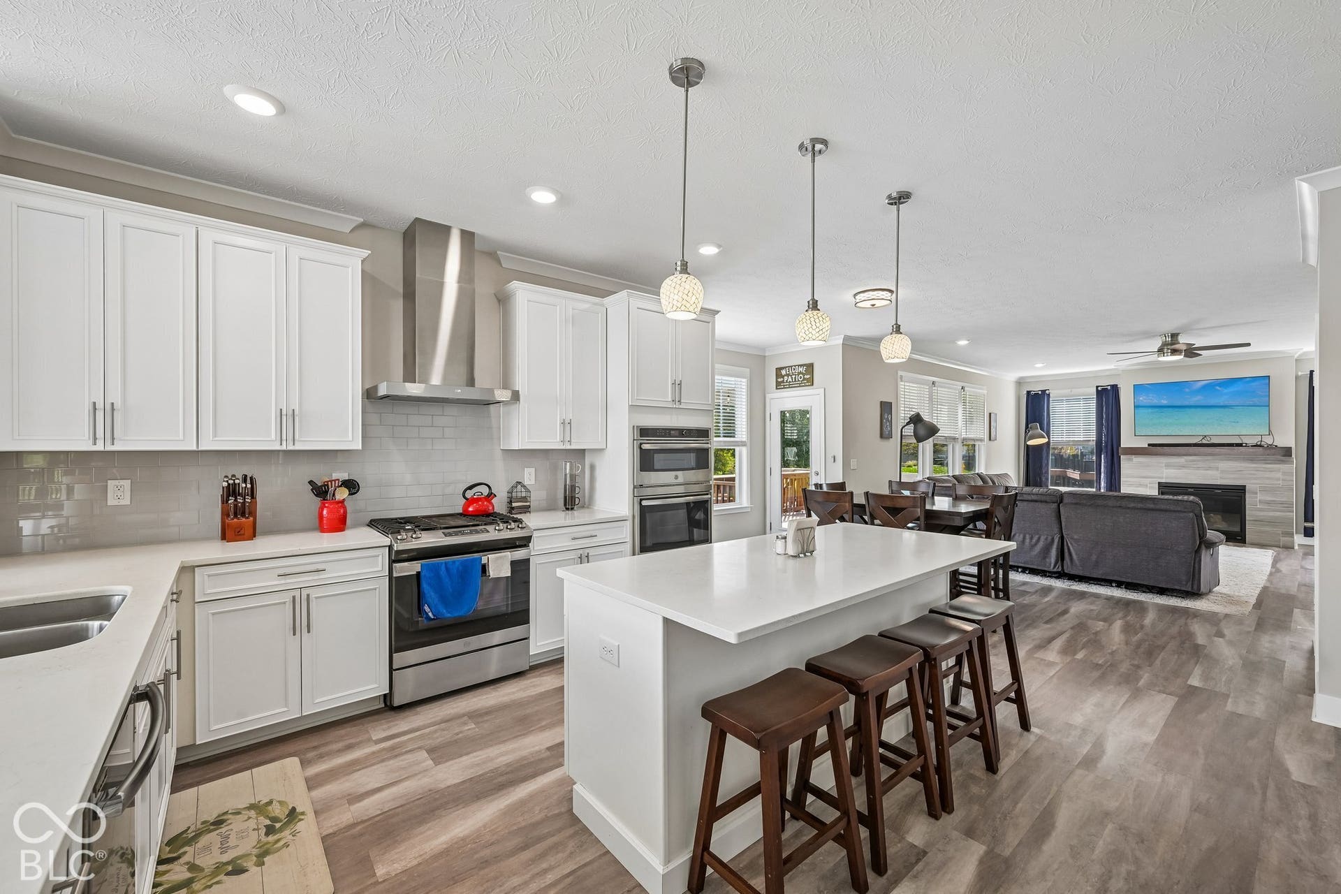 Kitchen featuring white cabinetry, stainless steel appliances, a center island with pendant lighting, and wood-finish flooring extending into the living area with a fireplace