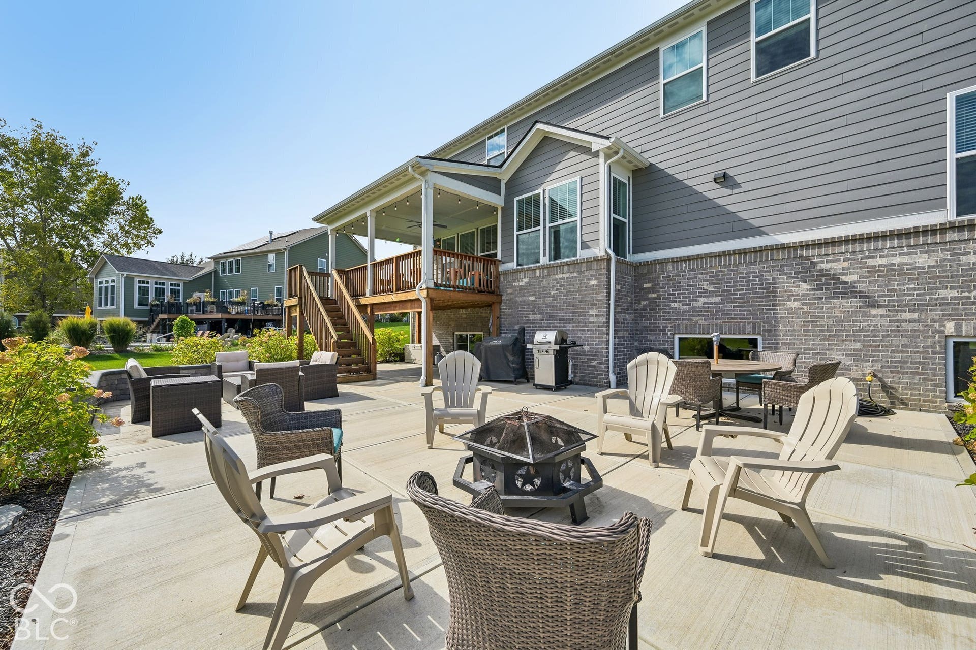 Spacious concrete patio with a fire pit area, covered porch with recessed lighting, and a multi-level deck with wooden railings