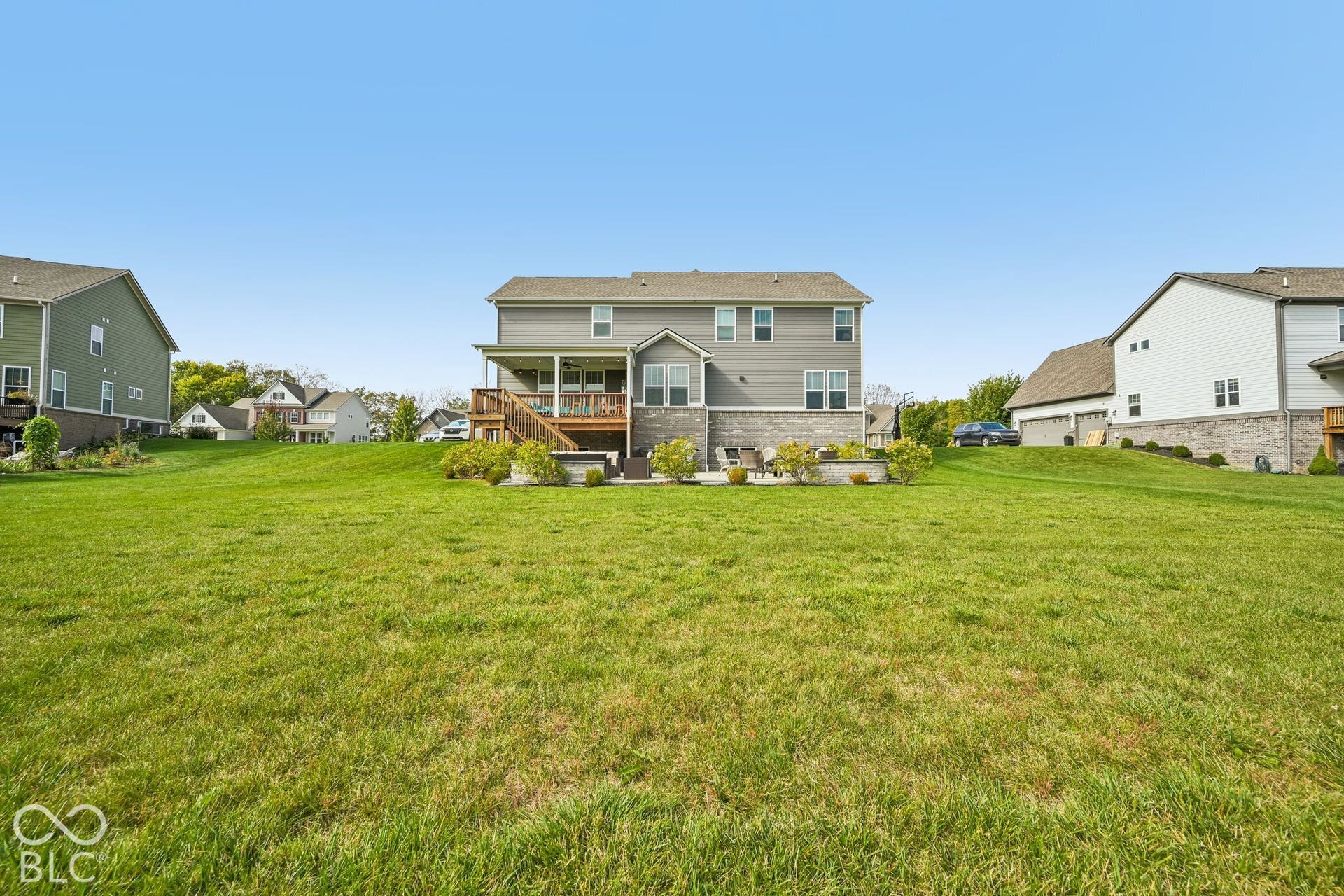 Expansive green lawn, covered deck, and lower stone patio