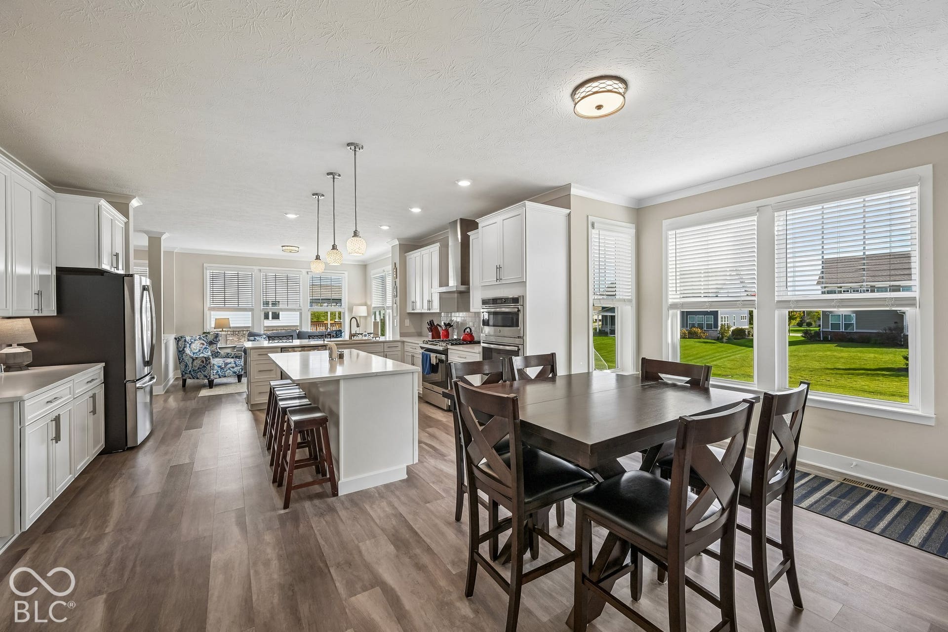 Expansive kitchen featuring wood-finish flooring, white cabinetry, a central island with seating, and stainless steel appliances