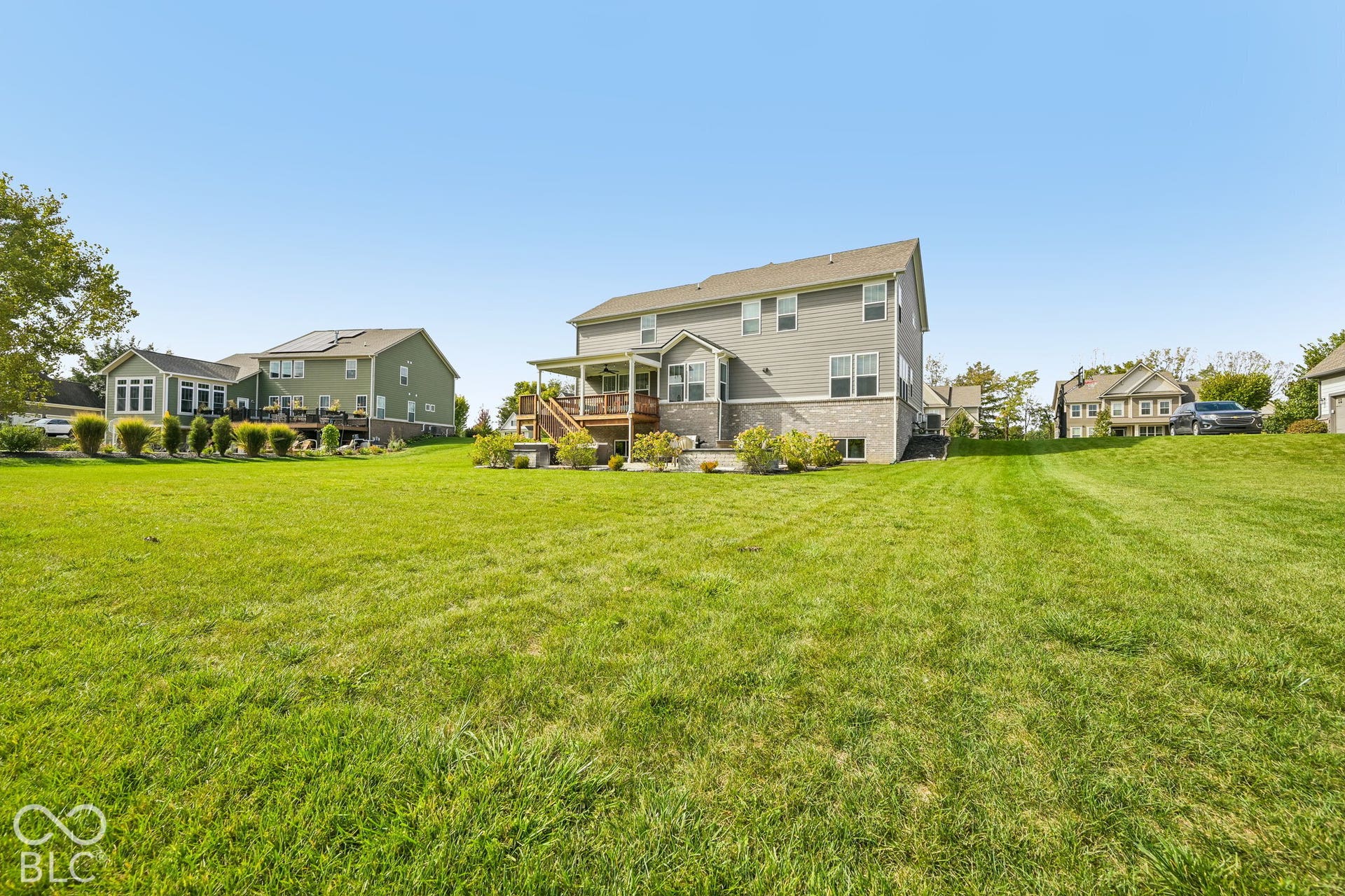 Expansive grassy yard leading to a residential structure with siding and a stone-finish foundation