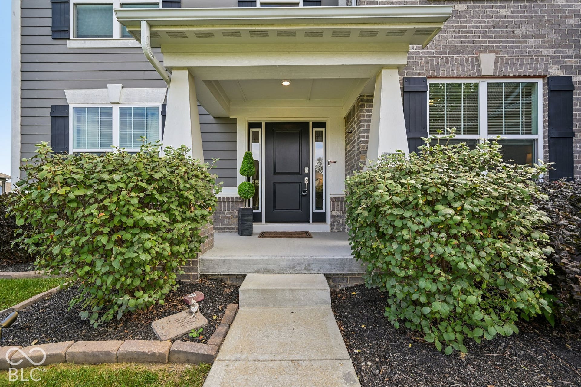 Brick and siding facade with dark shutters, covered entryway, and a paneled front door with sidelights