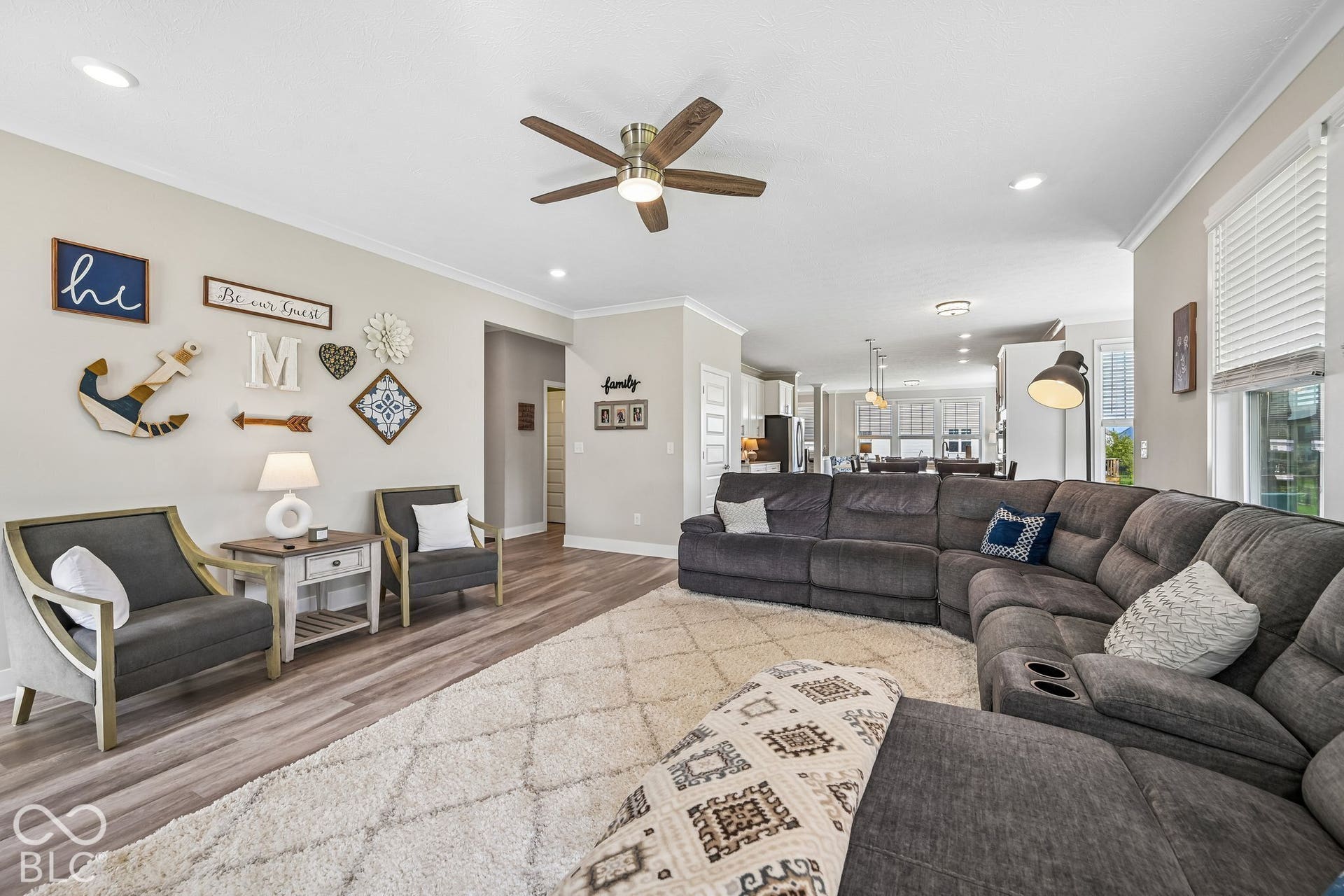 Wood-finish flooring throughout, recessed ceiling lighting, ceiling fan, crown molding, and an open layout providing a clear line of sight to the kitchen