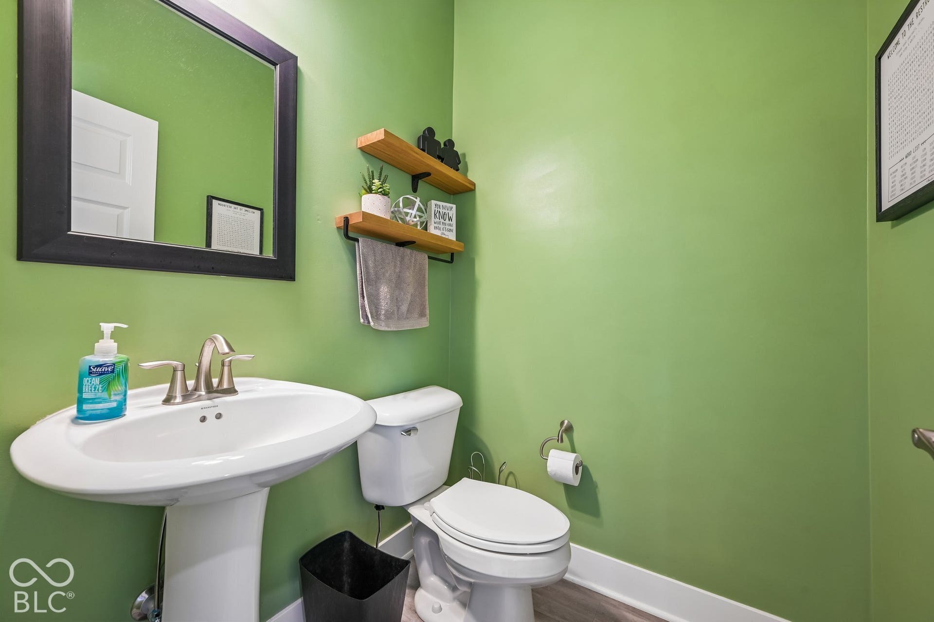 Pedestal sink with brushed nickel faucet, wall-mounted mirror with black frame, and two wood-finish wall shelves