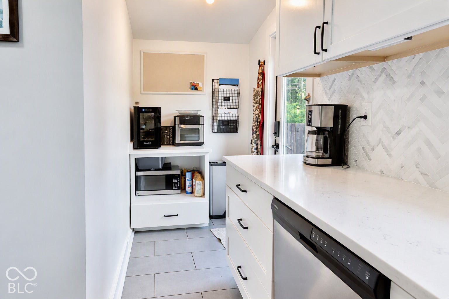White shaker-style cabinetry with black hardware, white countertops, herringbone tile backsplash, and stainless steel dishwasher