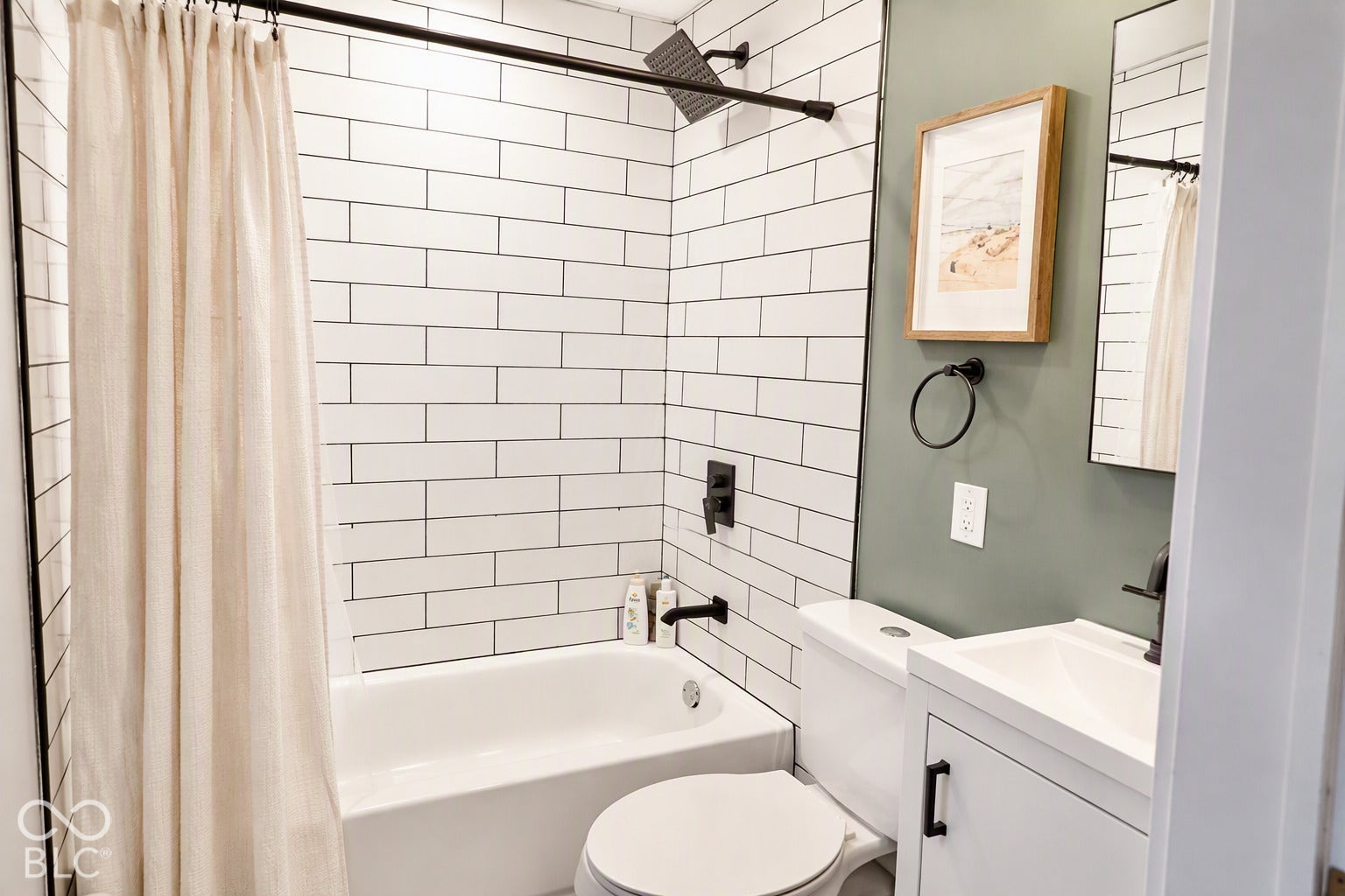White subway tile shower surround with dark grout, matte black shower fixtures, white bathtub, white vanity with integrated sink, and dark vanity hardware