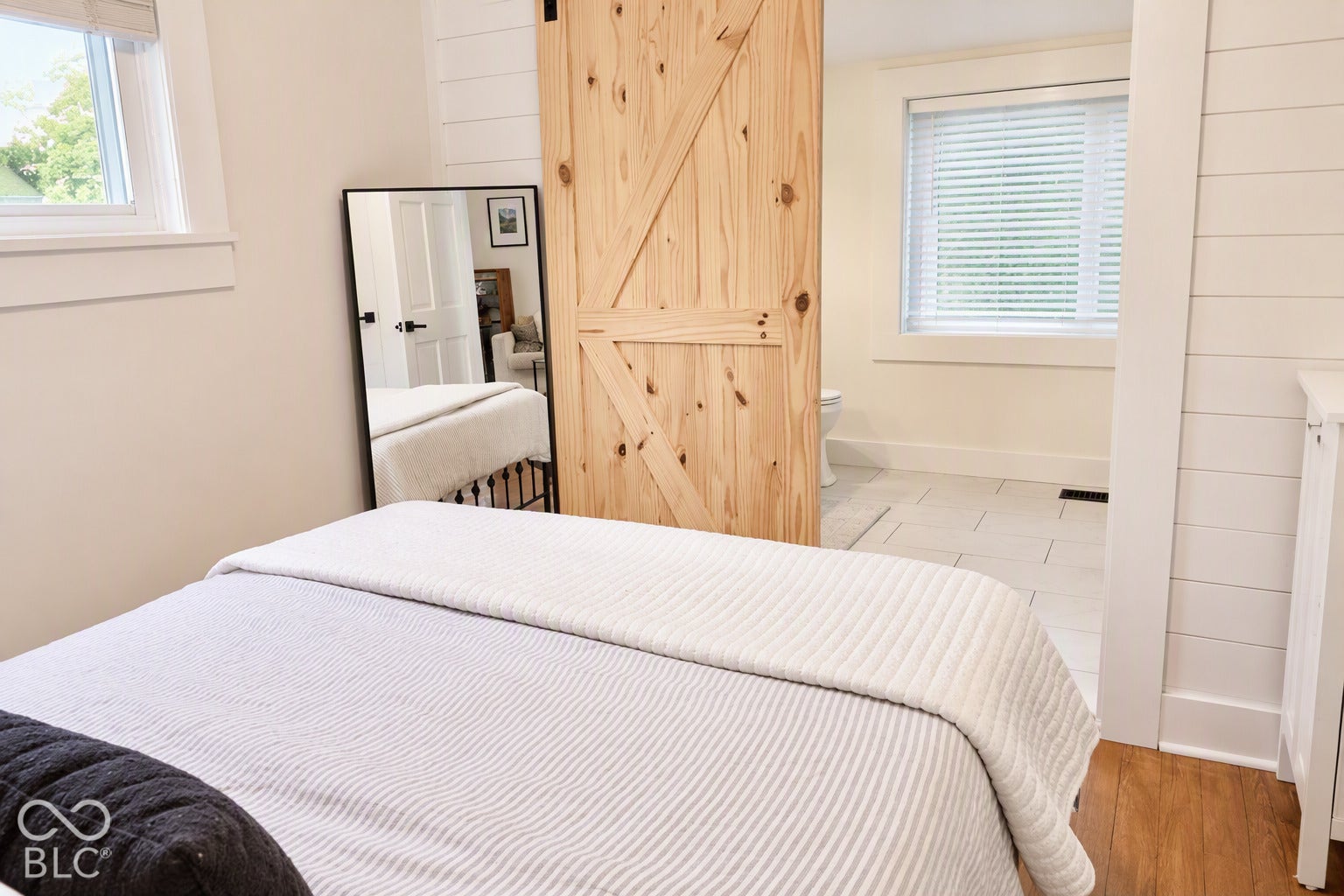 Wood-finish flooring, natural wood barn door, white plank wall, white trim accents, and a window with blinds