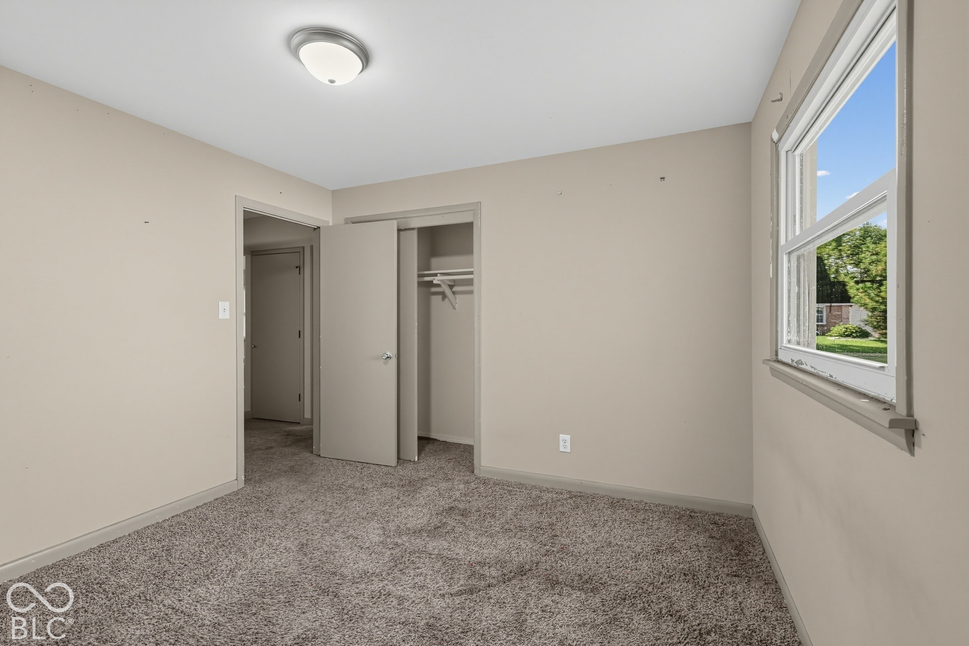 Plush carpet flooring, neutral wall paint, overhead flush-mount lighting, double-hung window, and a closet with a bi-fold door