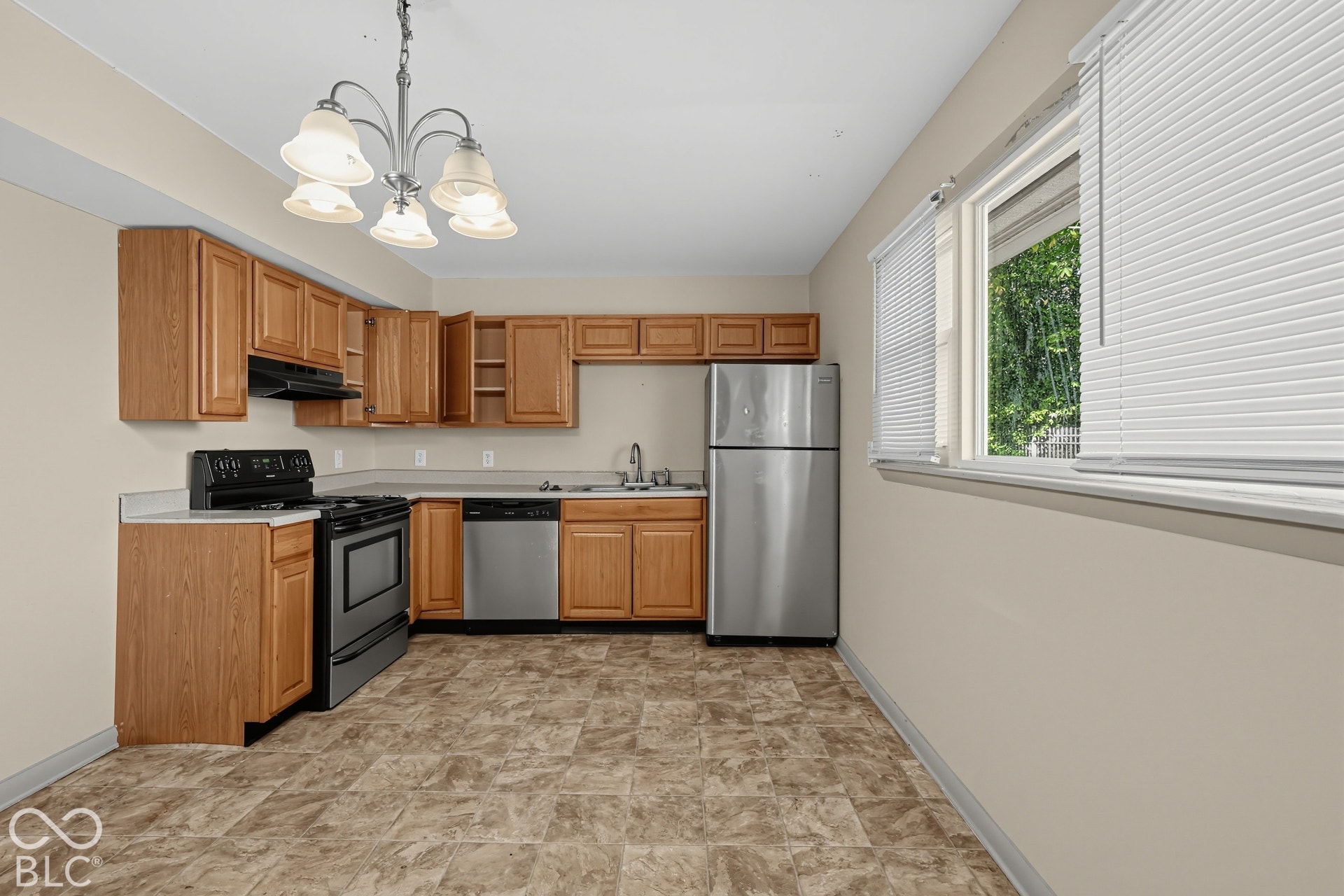 Kitchen featuring wood-finish cabinetry, stainless steel appliances, a five-bulb chandelier, and a large window