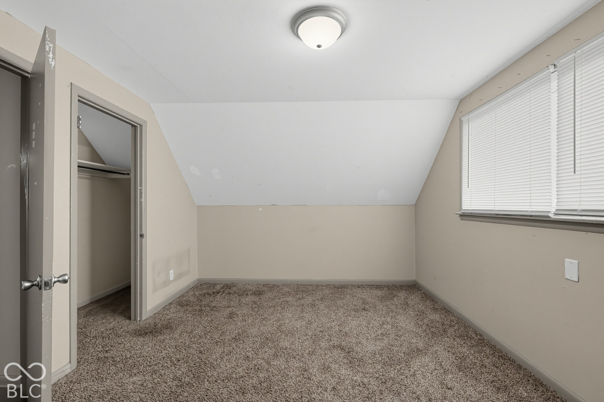 Carpeted room featuring a sloped ceiling, window with blinds, and flush-mount ceiling light