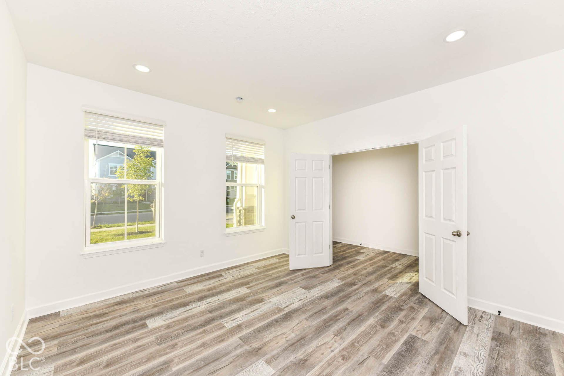 Recessed lighting, wood-finish flooring, two windows, neutral wall color, and double doors