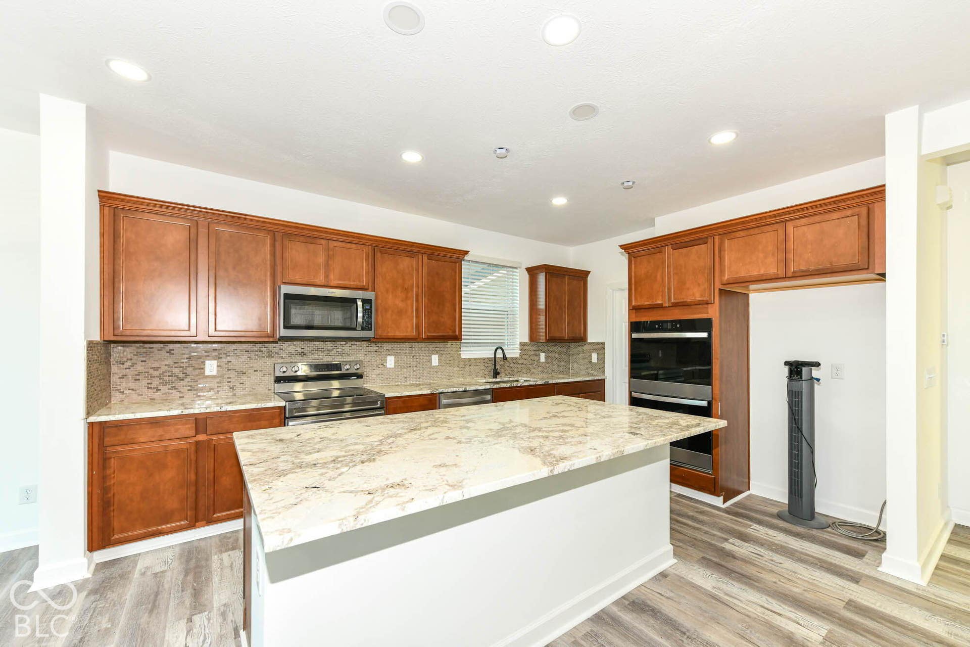 Kitchen featuring wood-finish cabinetry, a large center island with a light-toned countertop, stainless steel appliances, a tiled backsplash, and wood-finish flooring