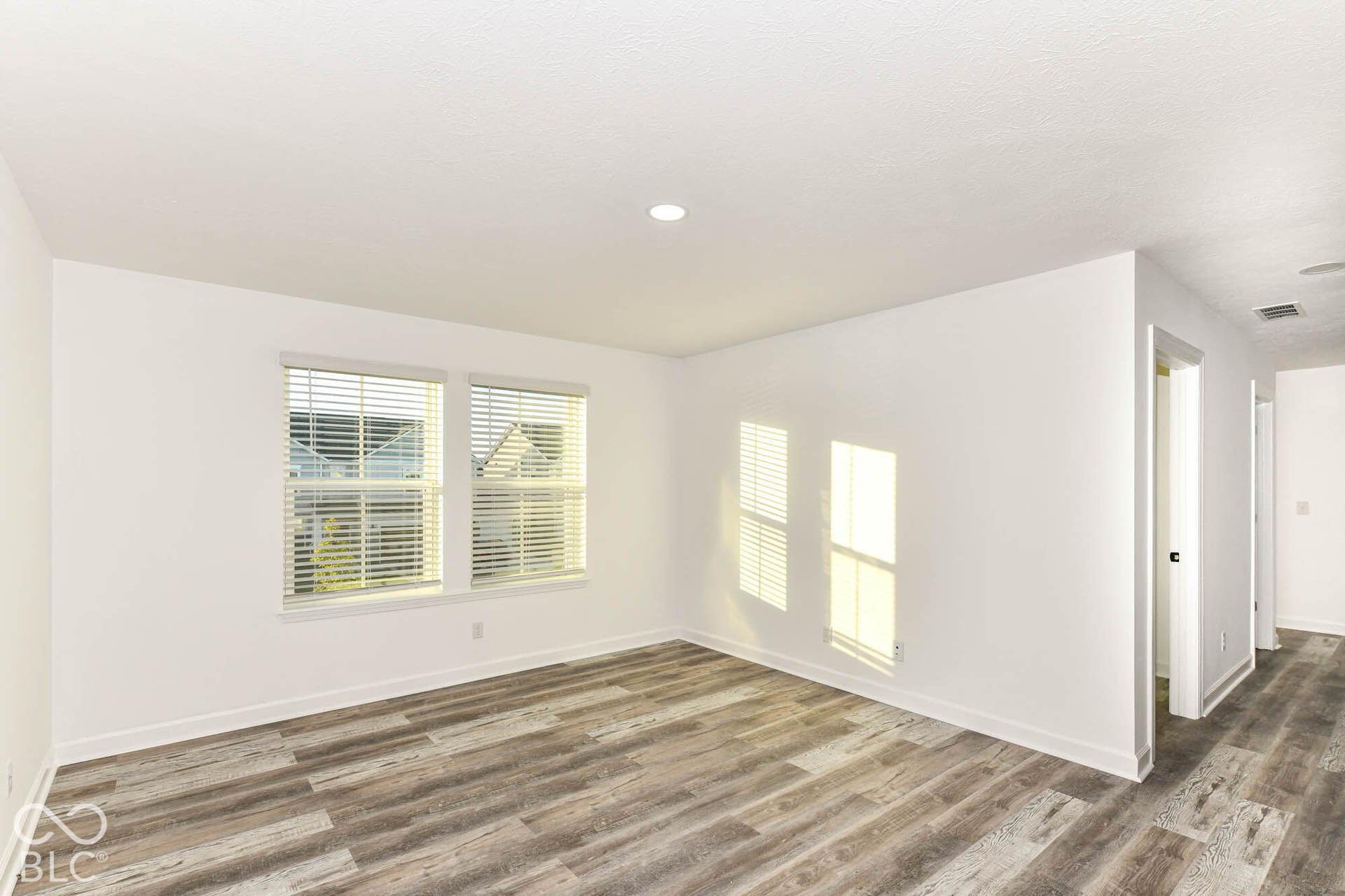 Recessed ceiling lighting, two windows with blinds, wood-finish flooring, white walls, and a white ceiling