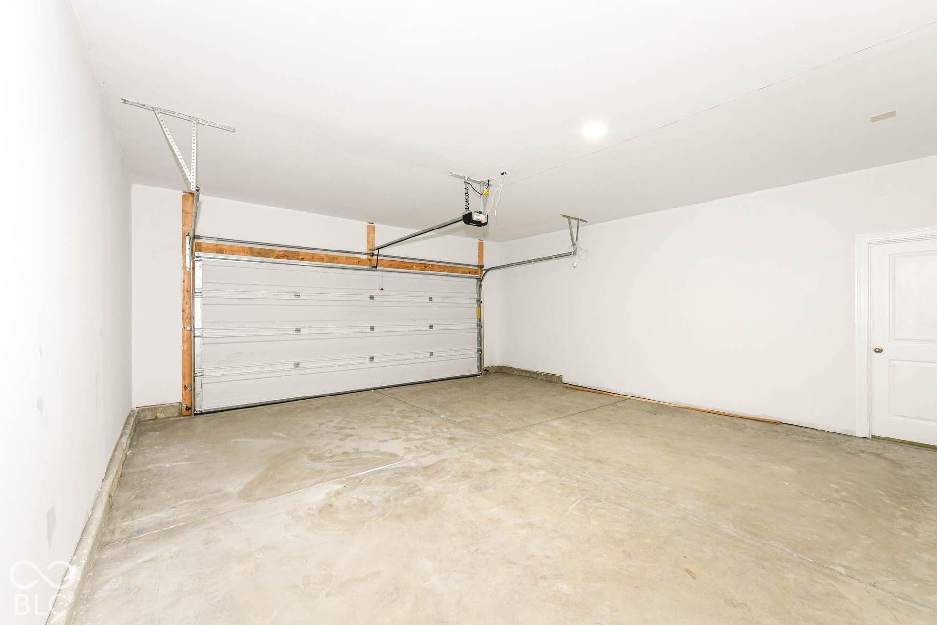 Attached garage with a sectional garage door, concrete flooring, and an interior door