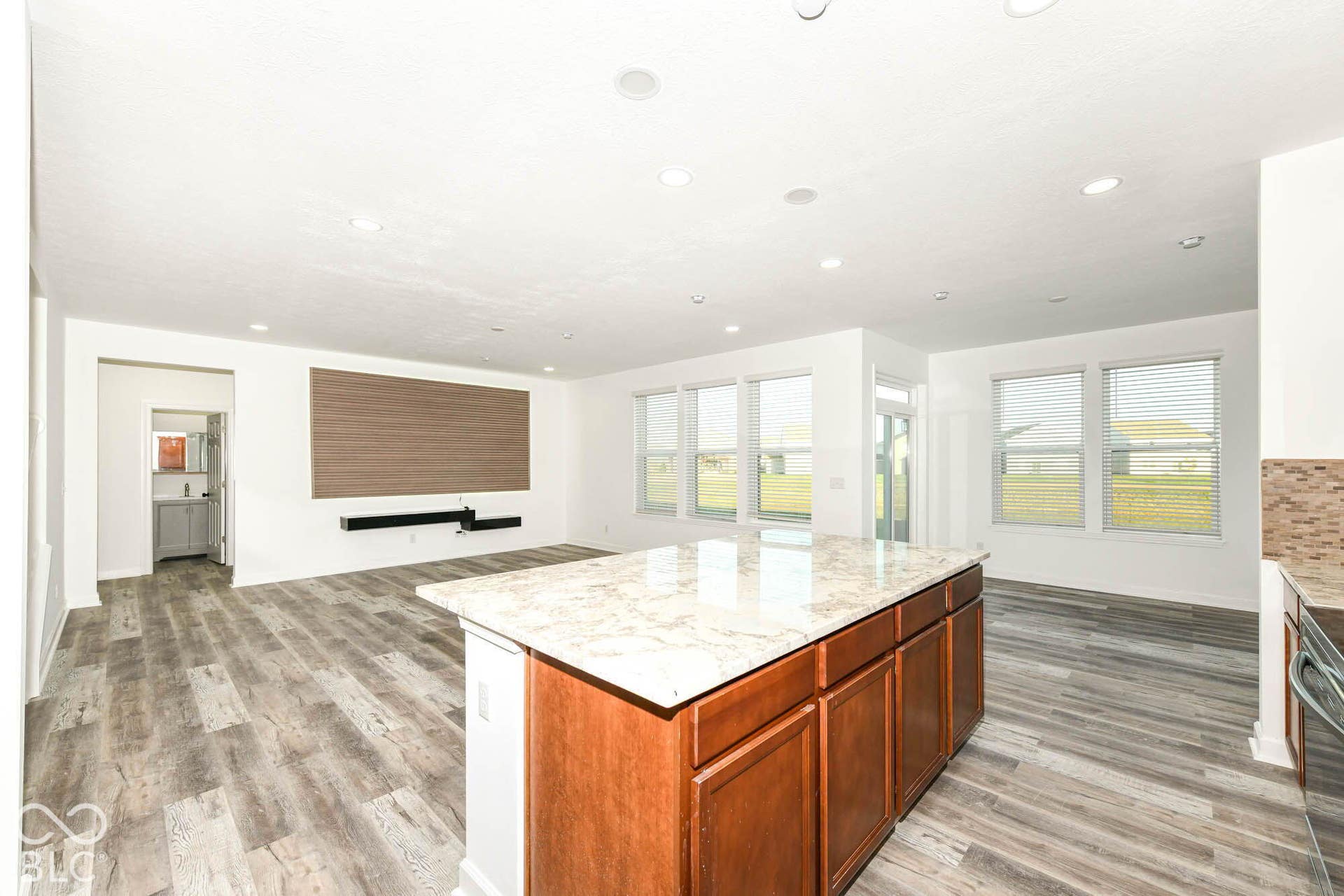Open-concept living space featuring wood-finish flooring, recessed lighting, a kitchen island with stone countertops, and multiple large windows
