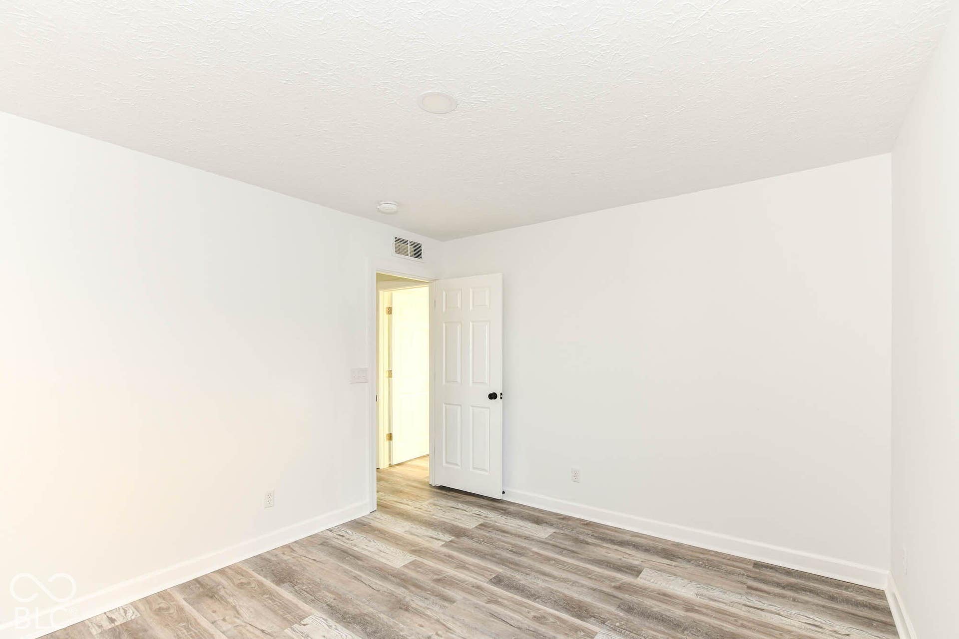 Light wood-finish flooring with white baseboards, a white door with a black knob, and a ceiling with a recessed light fixture