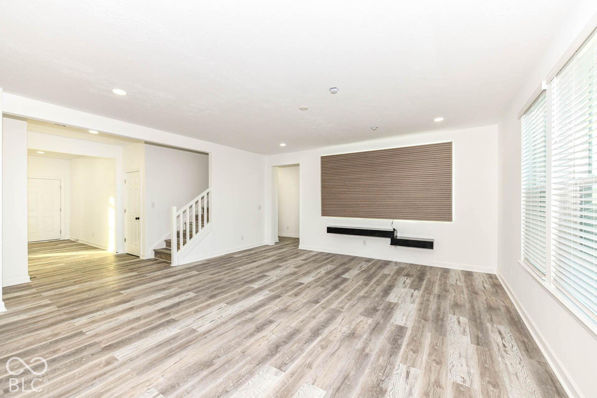 Recessed lighting, wood-finish flooring, white staircase with railing, window blinds, and a built-in wall unit