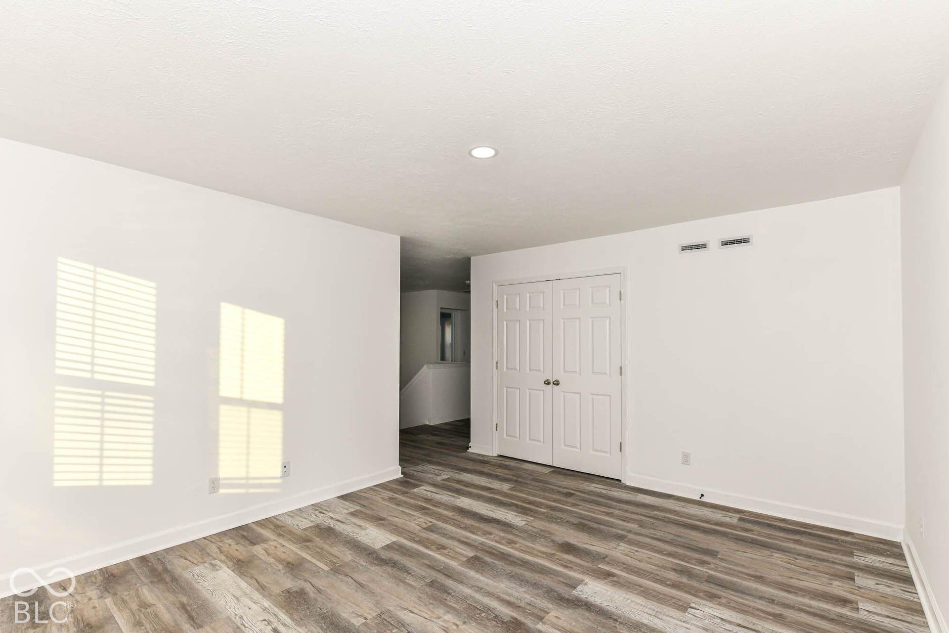 Wood-finish flooring throughout, bright white walls, recessed ceiling lighting, and a double-door closet