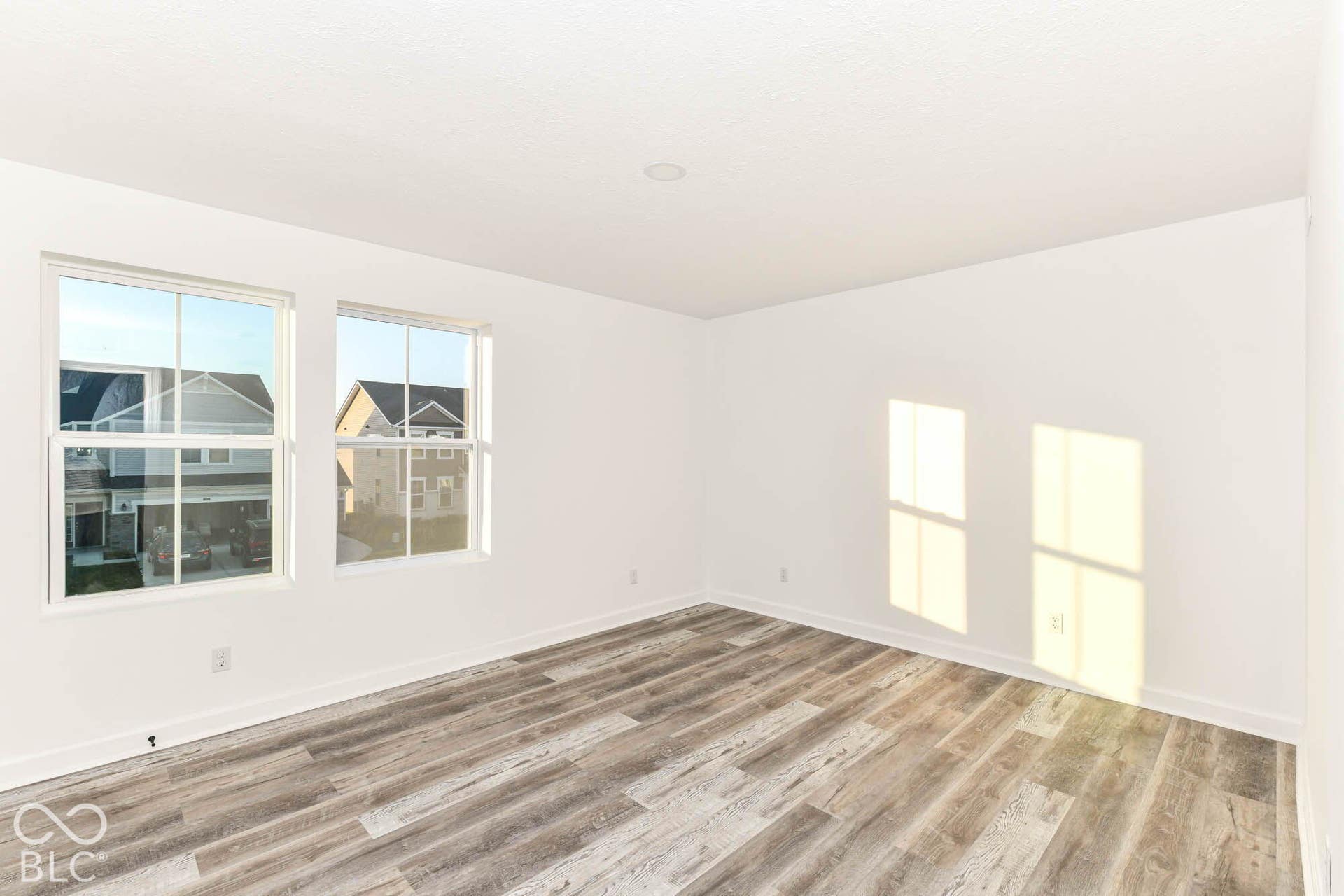 Recessed lighting with a flat white ceiling, white walls, two white-framed windows, and wood-finish flooring