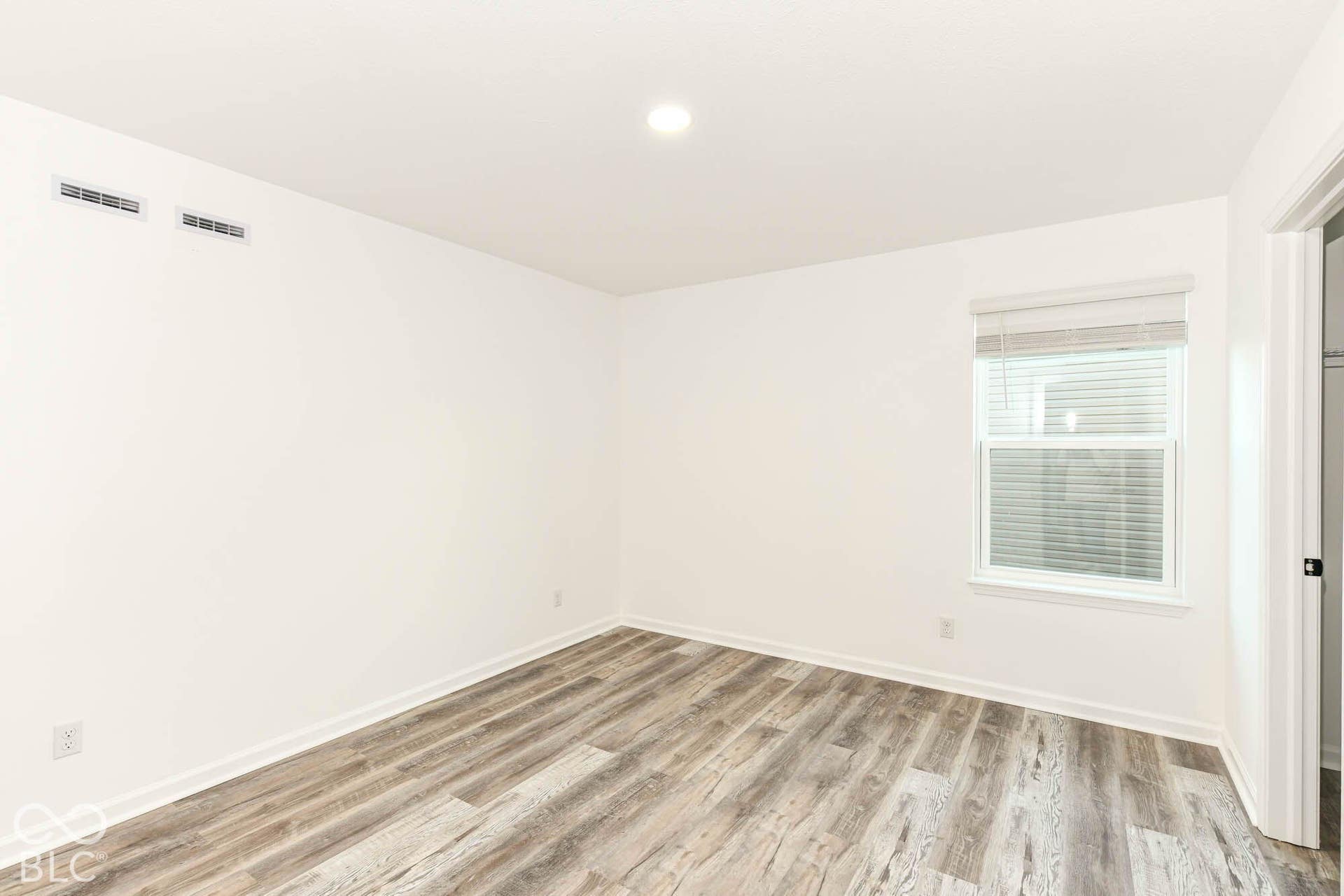 Wood-finish flooring with white baseboards, bright white walls, recessed ceiling lighting, and a window with blinds