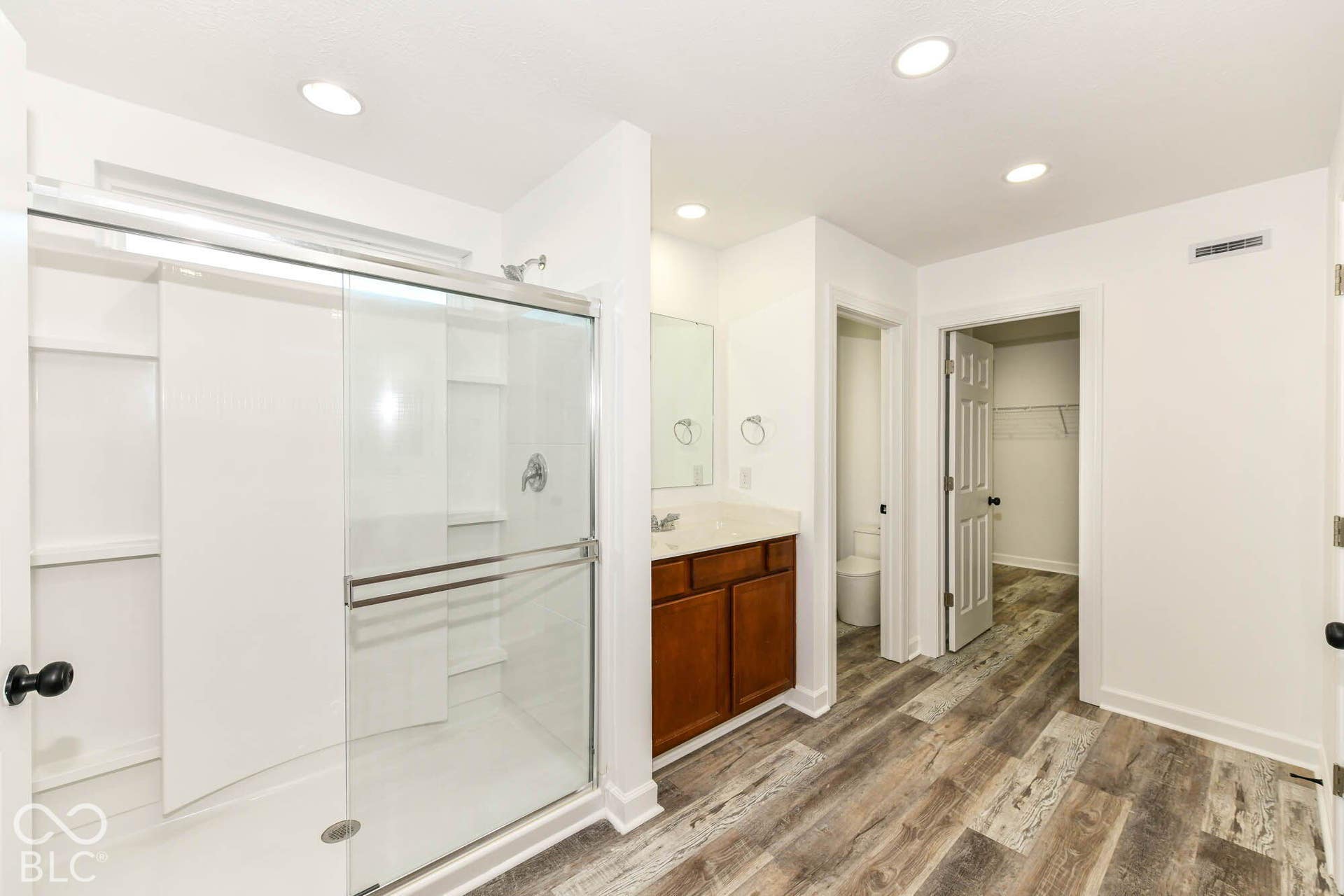 Sliding glass shower enclosure, single vanity with brown wood-finish cabinetry, light-toned countertop, recessed lighting, and wood-finish flooring