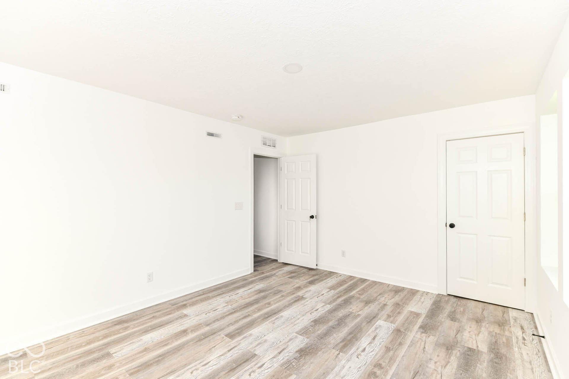Neutral white walls, wood-finish flooring, recessed ceiling lighting, and panel doors with matte black hardware