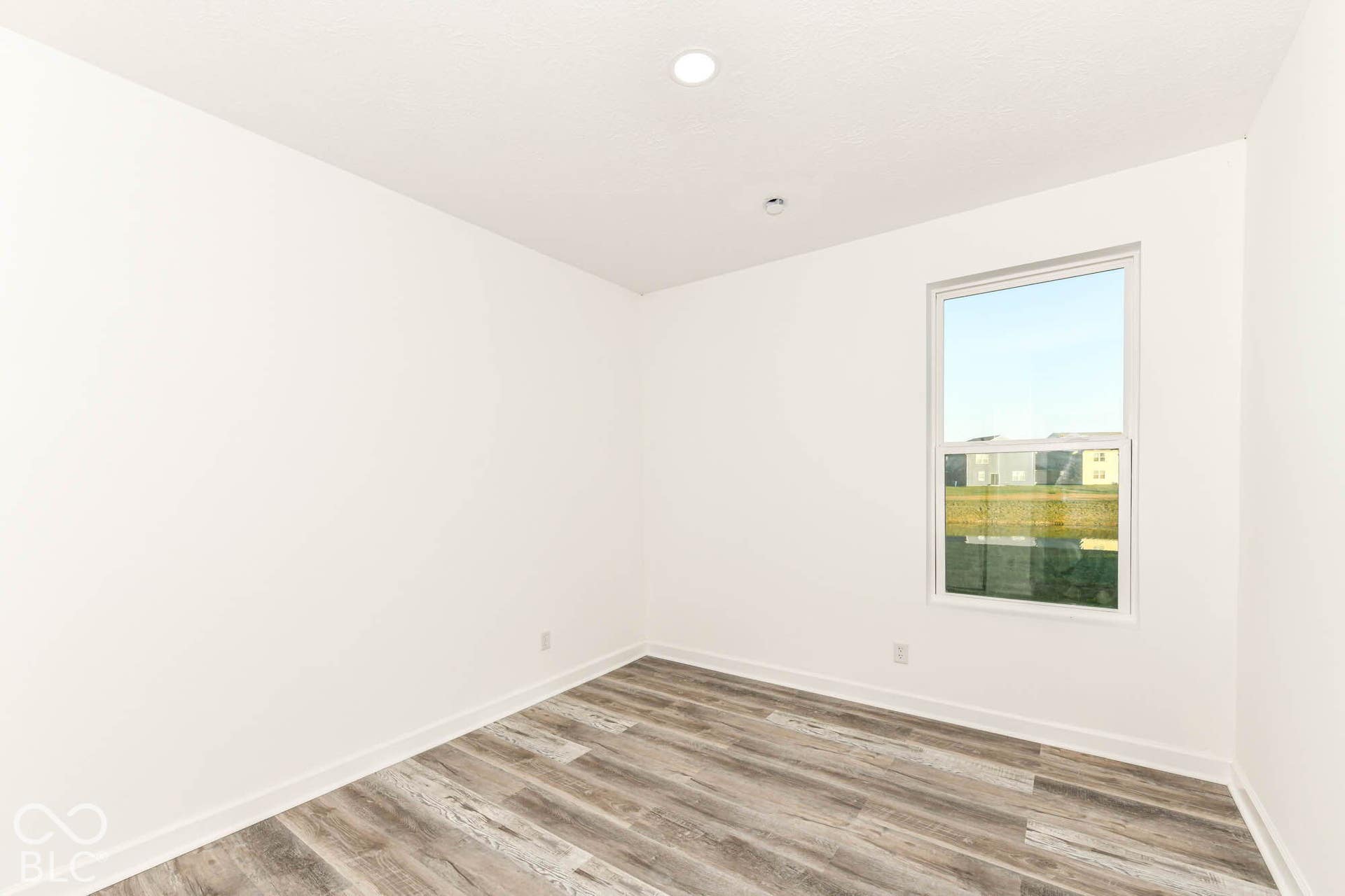 Wood-finish flooring with white baseboards, a single window, and recessed ceiling lighting