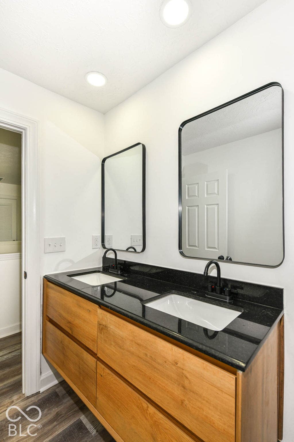 Dual rectangular undermount sinks set in a dark countertop, complemented by two framed mirrors and matte black faucets