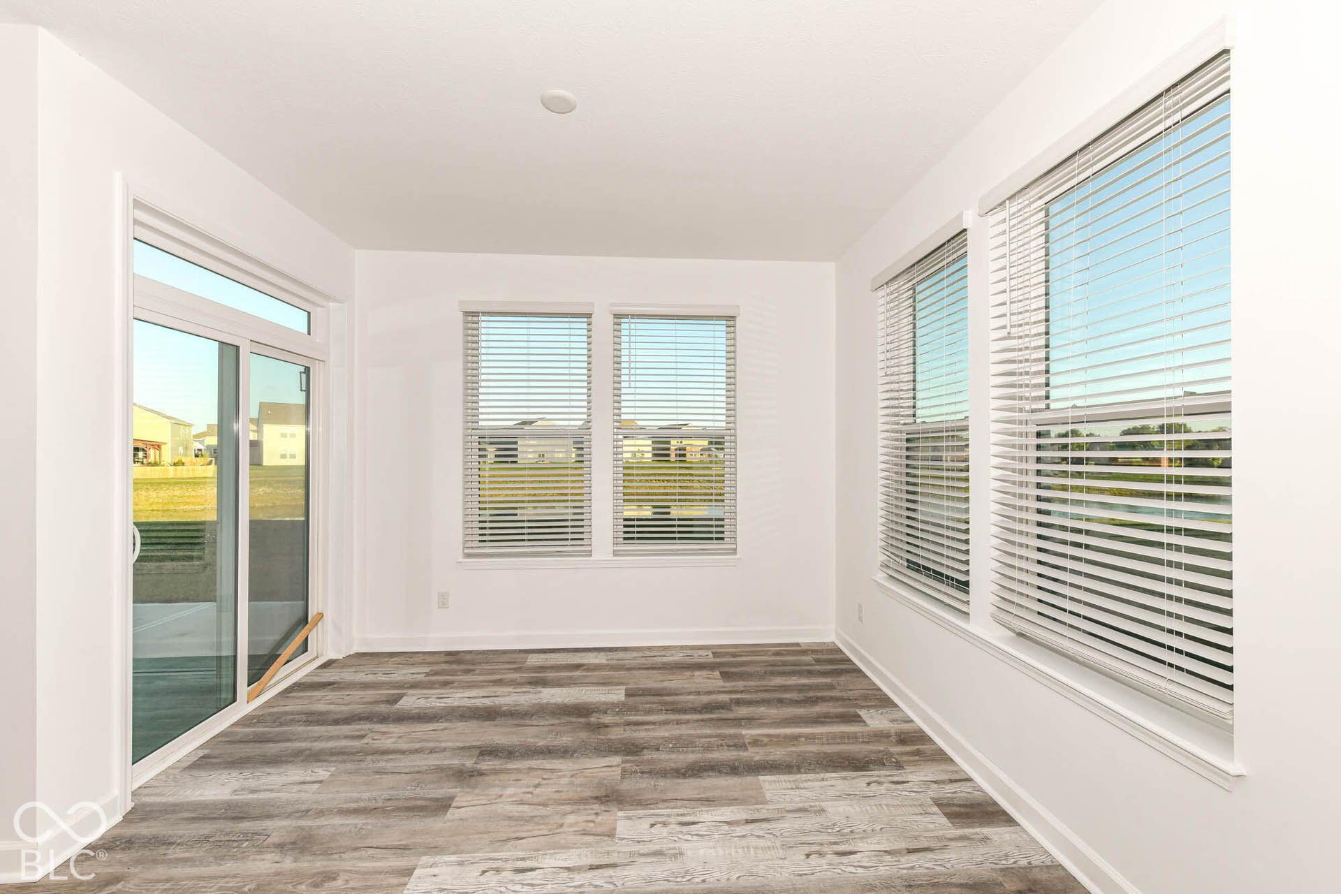 Spacious room with wood-finish flooring, multiple windows, and a sliding glass door