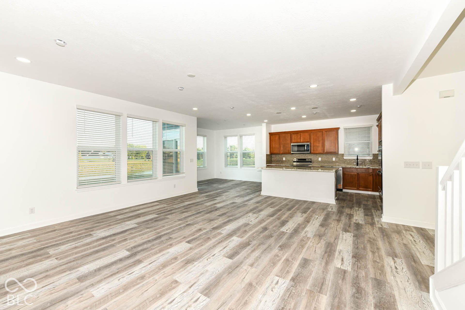 Spacious open-concept living area featuring wood-finish flooring, recessed lighting, and multiple windows with blinds