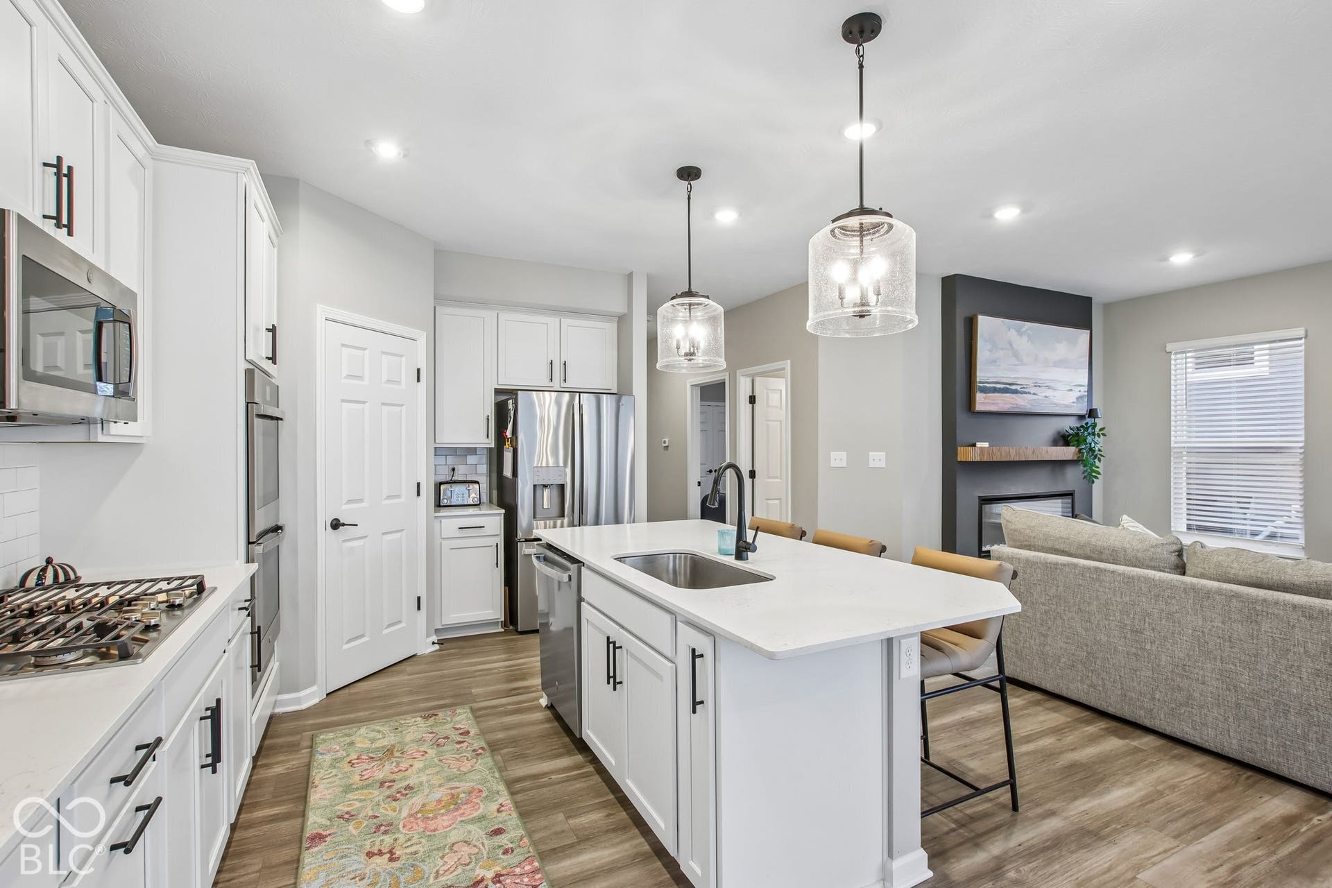 Kitchen featuring white cabinetry, stainless steel appliances, a center island with sink, pendant lighting, and wood-finish flooring