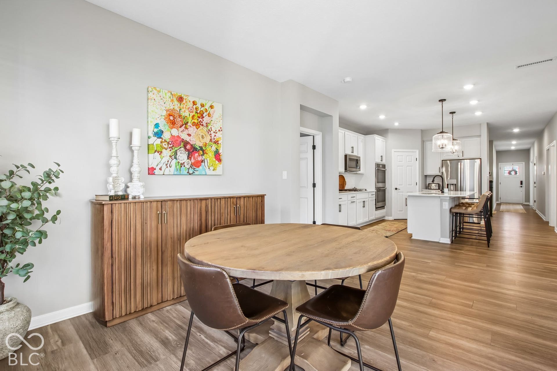 Open-concept floor plan featuring wood-finish flooring, recessed lighting, and a kitchen with white cabinetry, stainless steel appliances, and a central island with pendant lighting