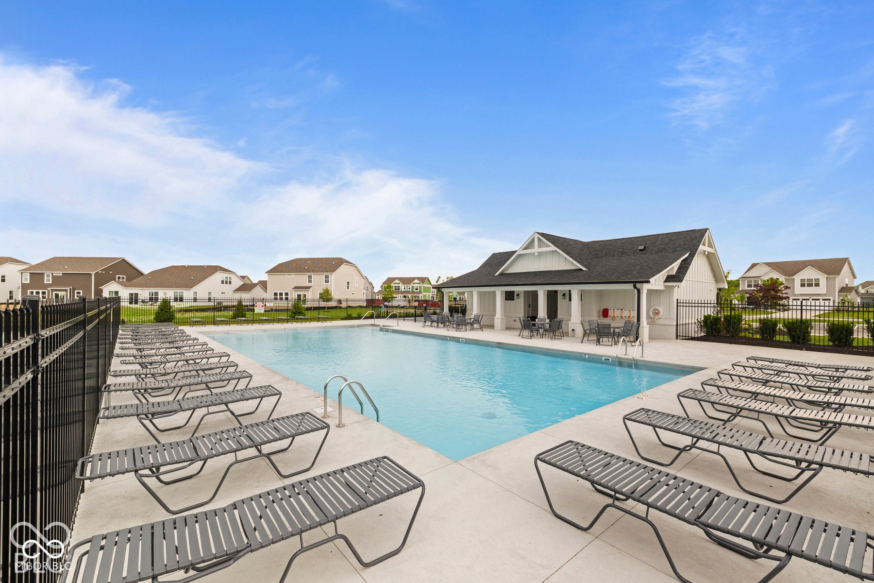 Expansive outdoor swimming pool with surrounding concrete decking, multiple lounge chairs, and a white clubhouse structure featuring a covered patio