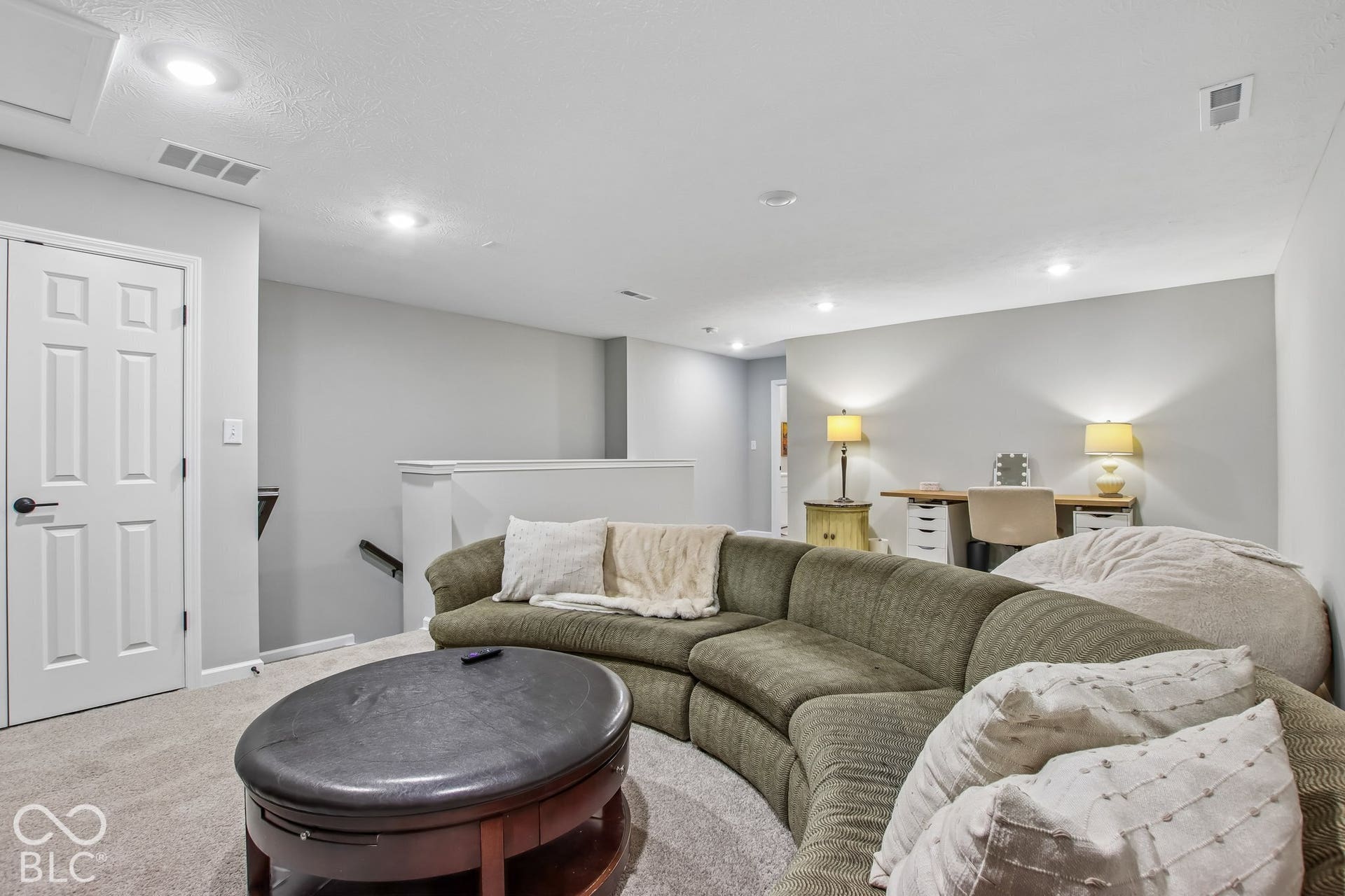 Finished basement recreation room featuring a curved sectional seating area, recessed ceiling lighting, neutral carpet flooring, and accent lighting from table lamps