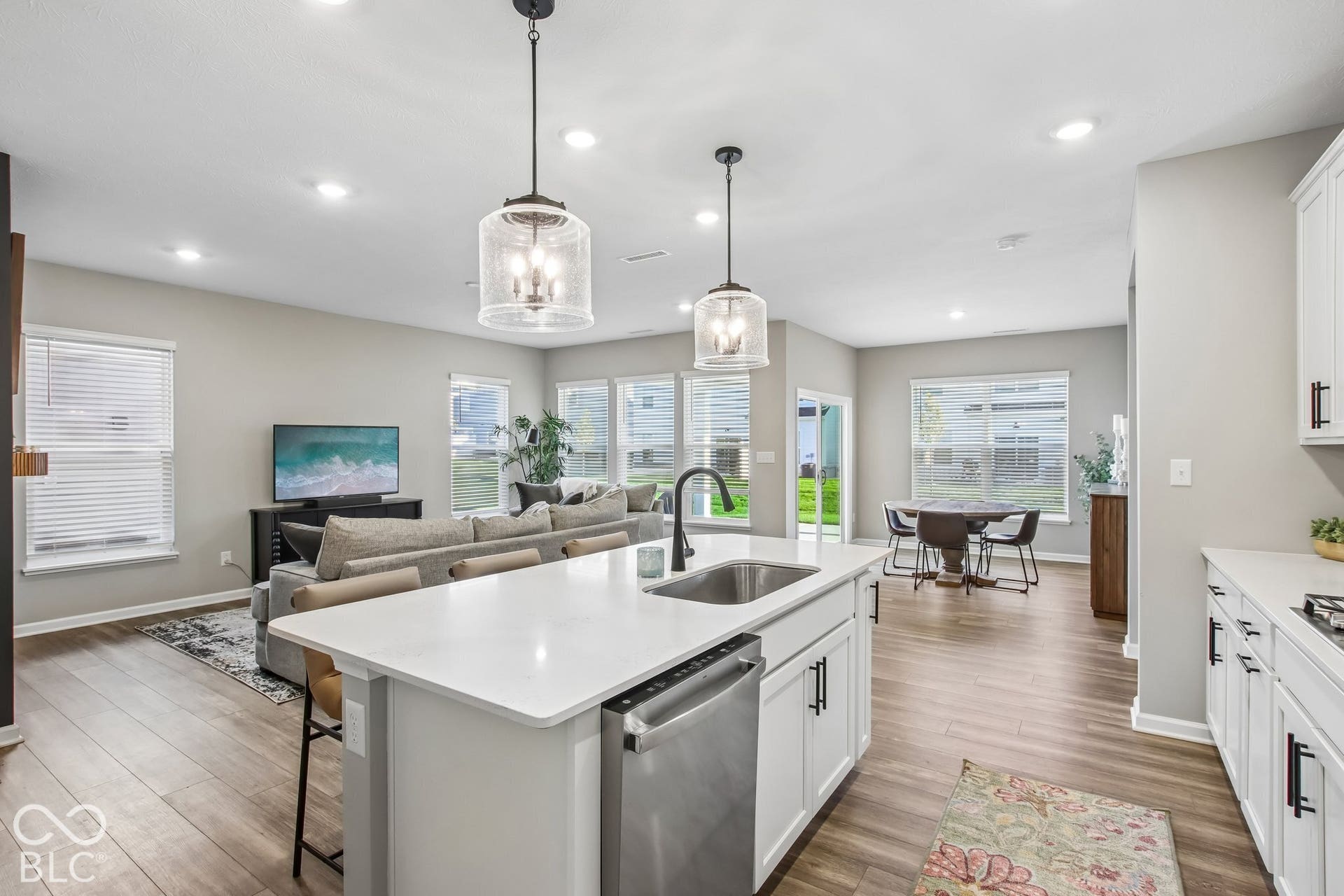 Kitchen island featuring a stainless steel sink and dishwasher, pendant lighting, white cabinetry, and wood-finish flooring
