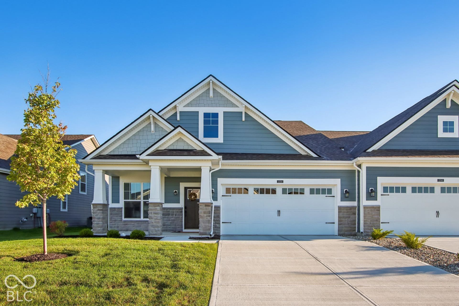 Exterior featuring blue siding, stone facade accents, a front porch with white columns, an attached garage, and a concrete driveway