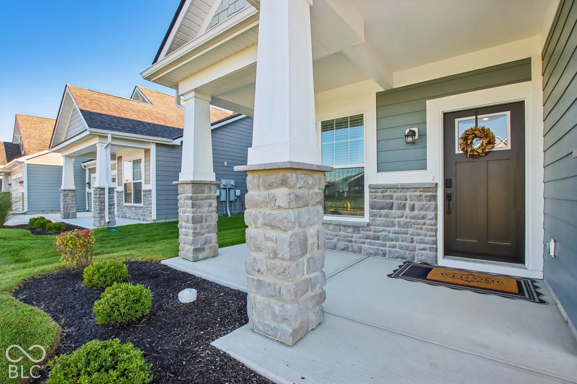Stone-wrapped porch columns, horizontal siding, and a dark entry door with a window pane