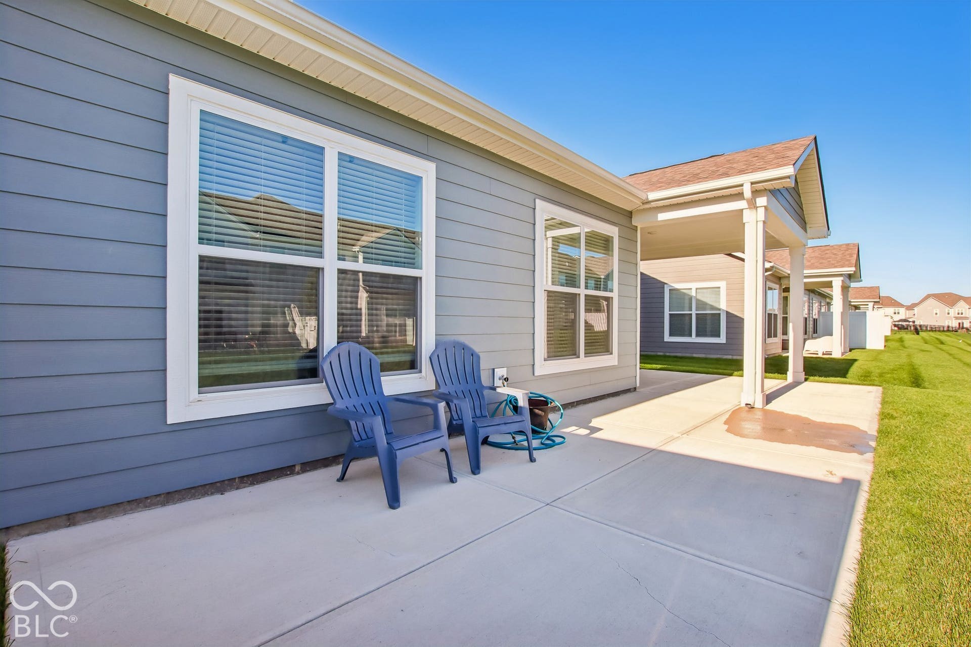 Expansive concrete patio with direct access to the home's exterior, featuring large multi-pane windows and glass sliding doors