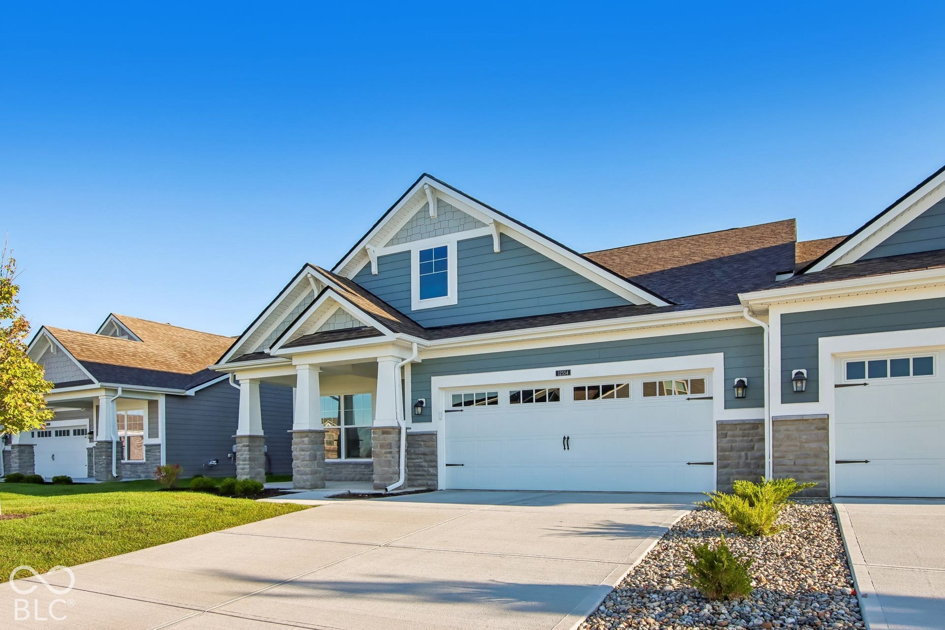 Exterior featuring blue siding, white trim, stone accents, gabled rooflines, and a two-car garage with decorative hardware