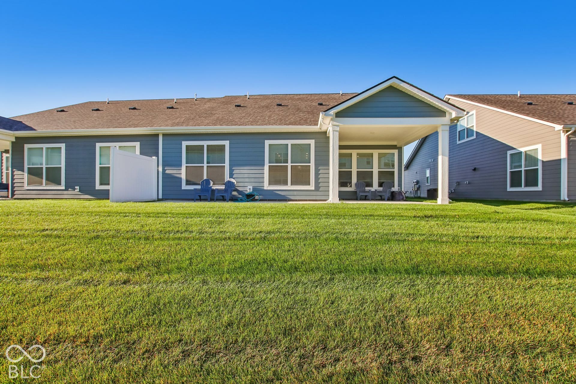 Expansive green lawn, covered patio, white window trim, and a prominent gable roofline