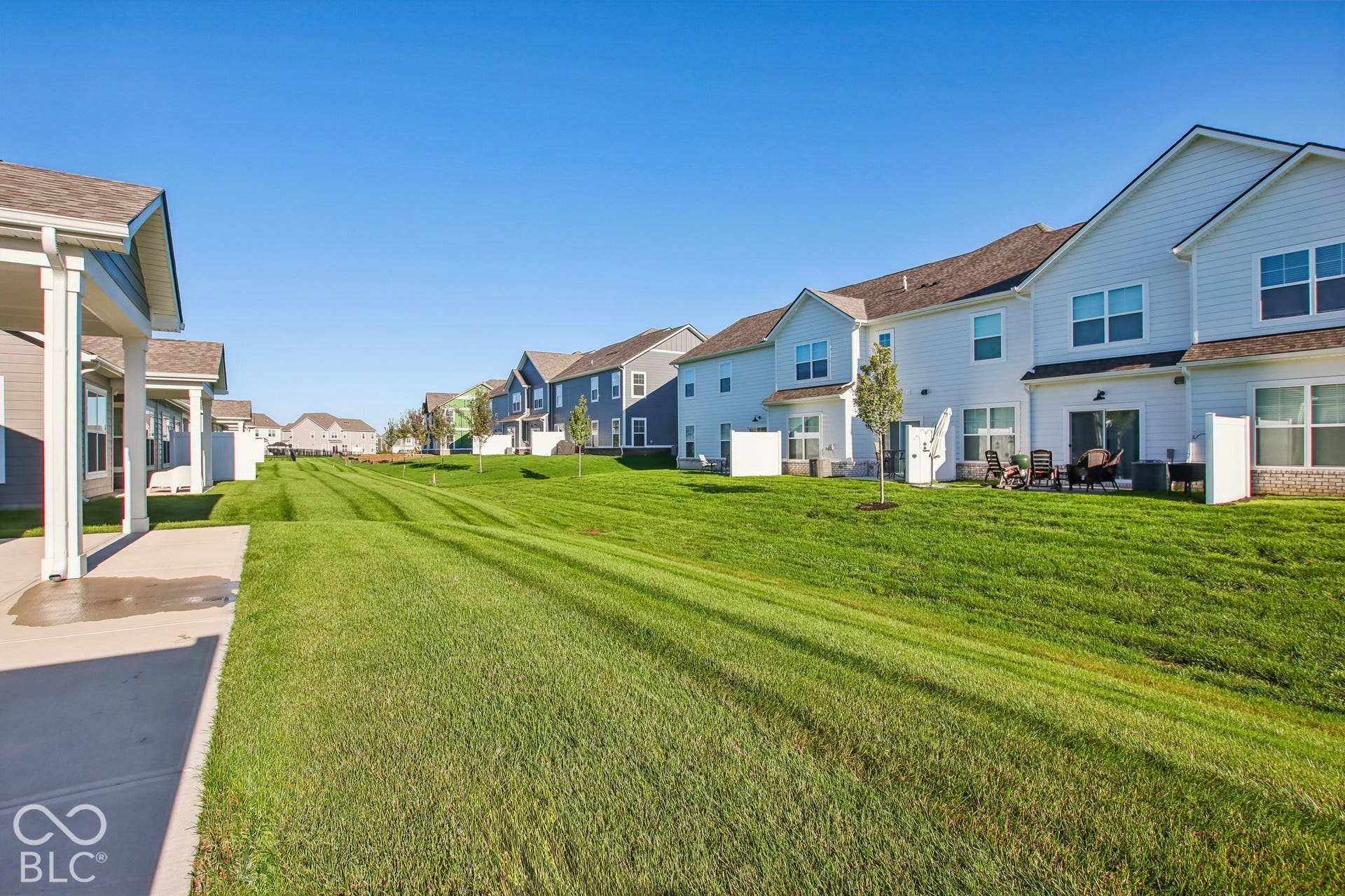 Expansive manicured lawn with defined mowing patterns, bordered by contemporary multi-story residences featuring varied exterior finishes in blues and whites