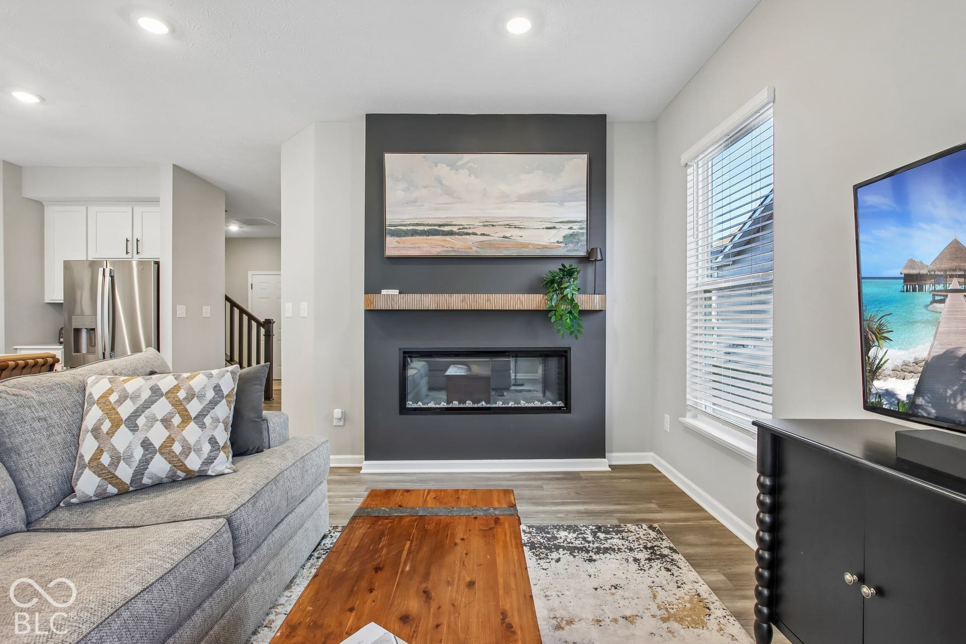 Central living area featuring a linear electric fireplace, wood-finish flooring, recessed lighting, and a window with blinds