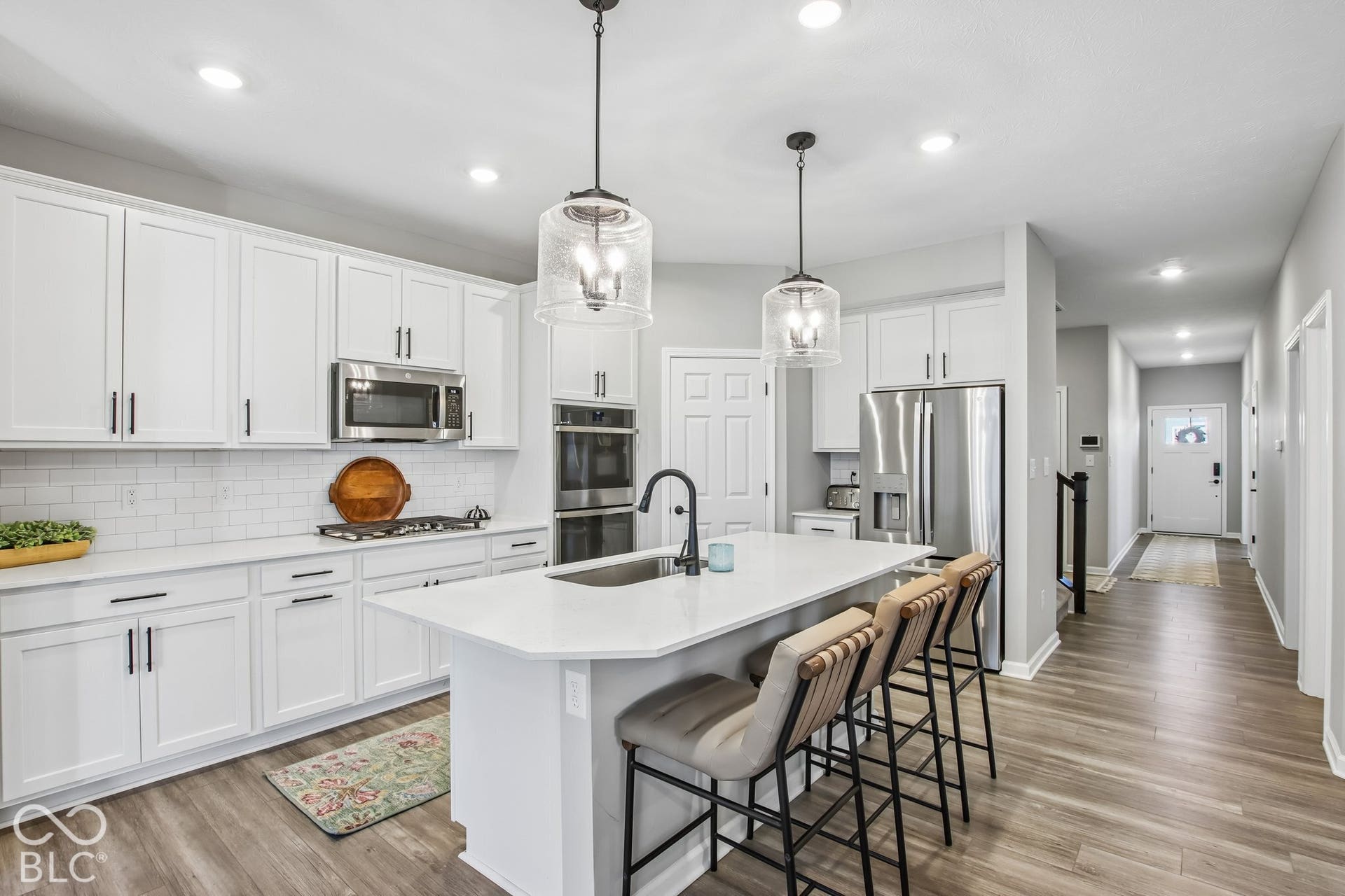 Kitchen with white cabinetry, stainless steel appliances, a center island with sink, pendant lighting, and wood-finish flooring