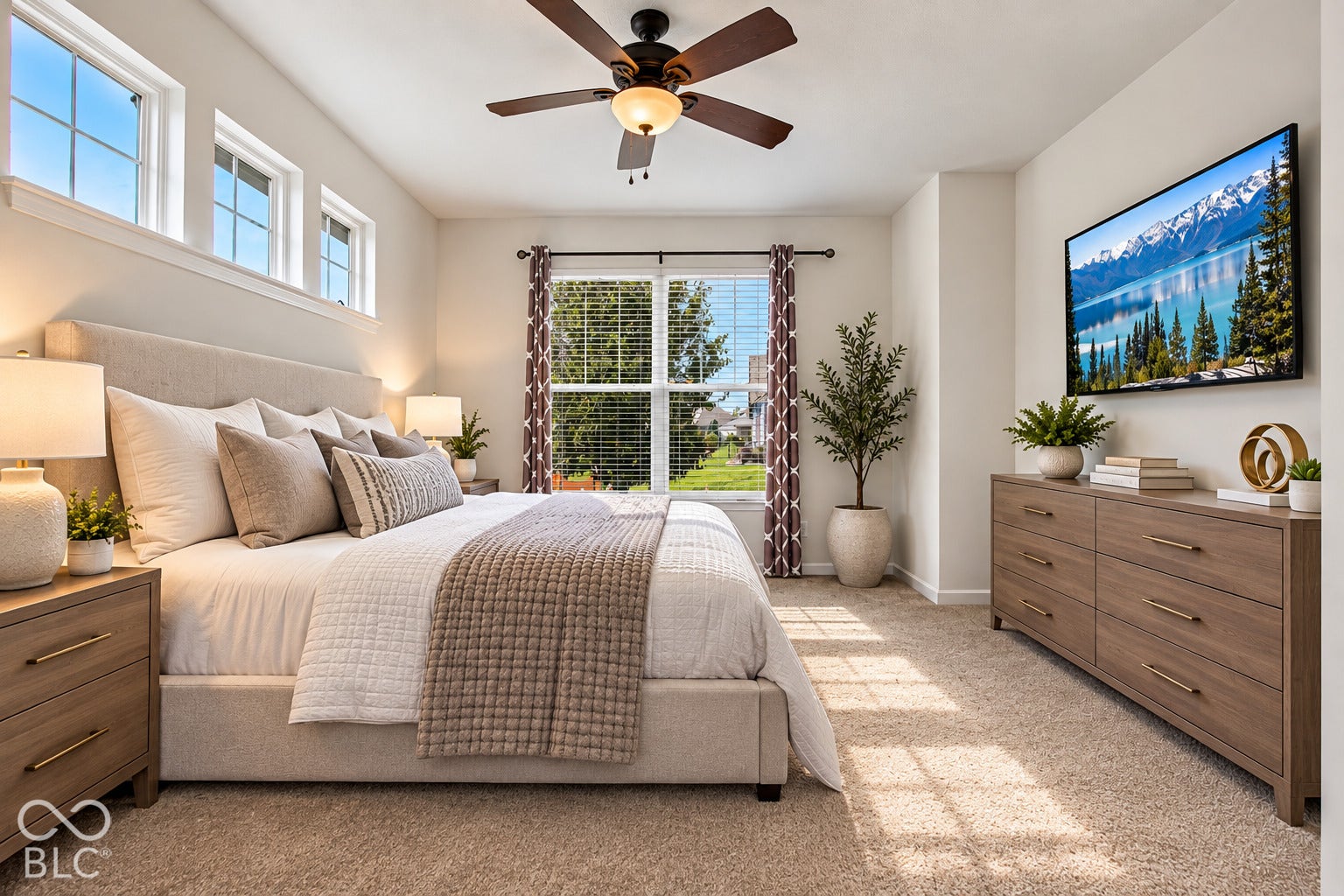 Ceiling fan with integrated lighting, multiple windows providing natural illumination, neutral-toned carpet flooring, and an upholstered bed frame