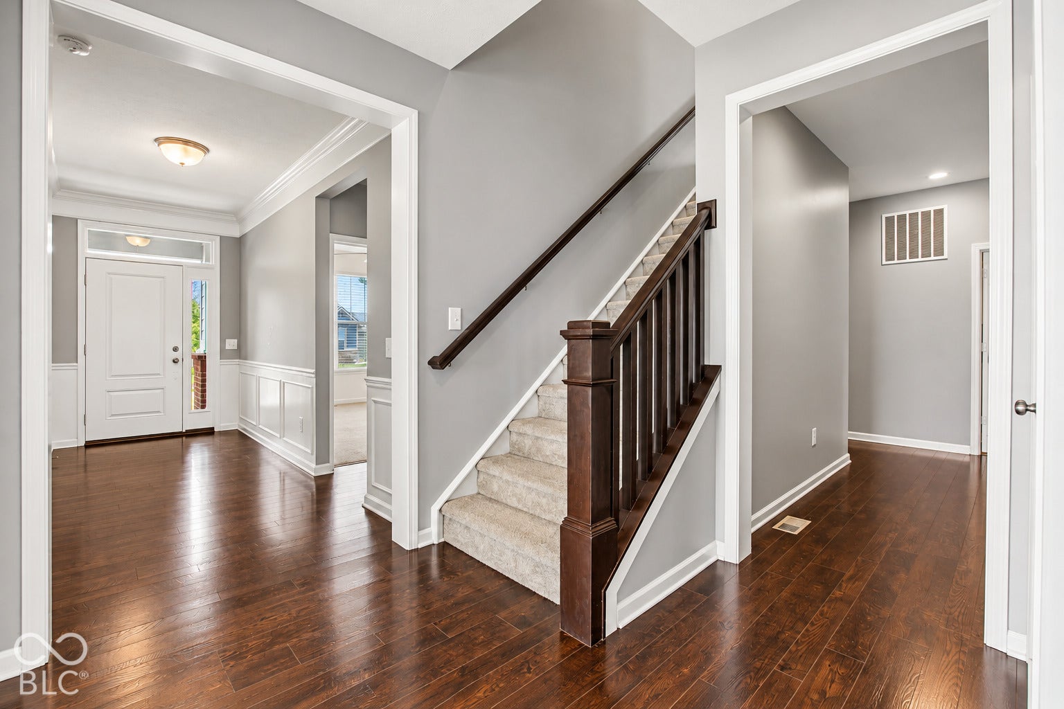 Hardwood flooring throughout the entry, staircase with wood newel post and railings, wainscoting details, and recessed lighting in the hallway