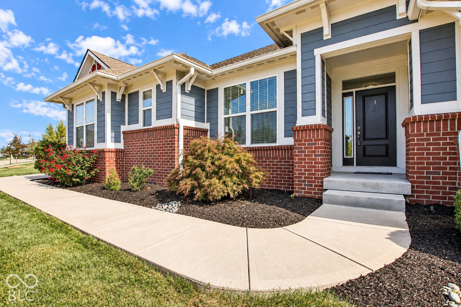 Brick and siding exterior with decorative corbels, concrete walkway, and landscaped garden beds