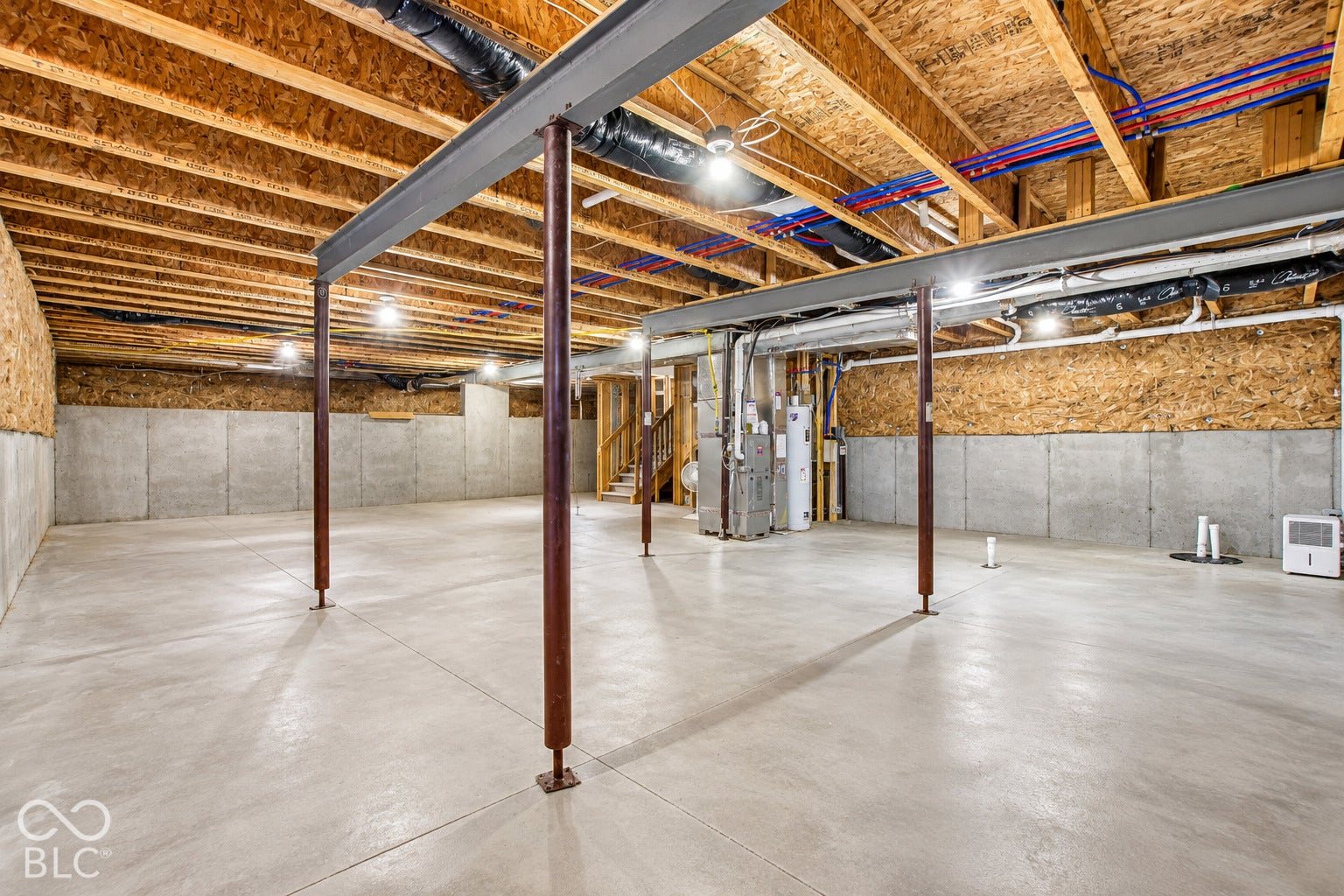 Expansive unfinished basement featuring concrete flooring, exposed ceiling joists, support beams, and built-in lighting