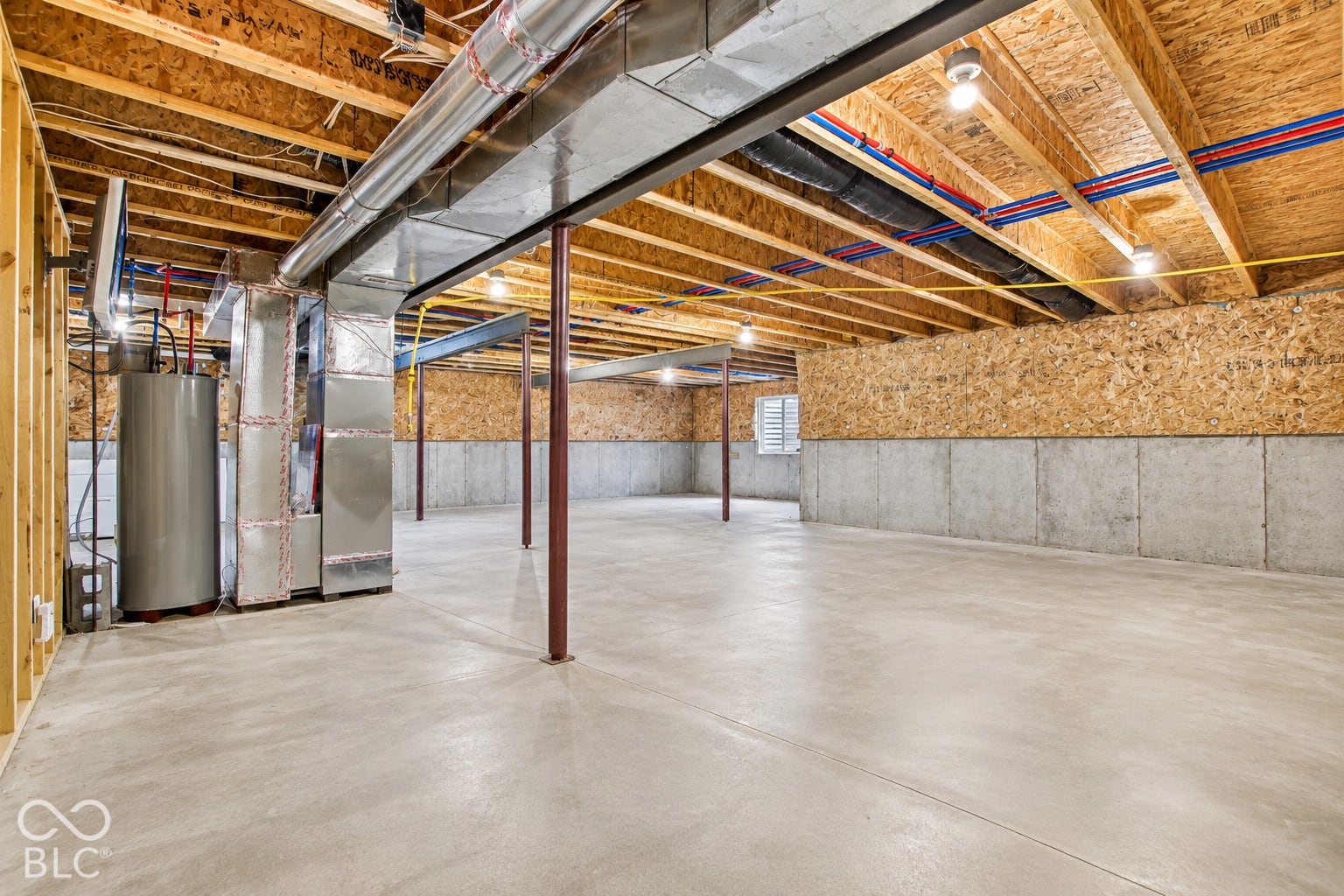Expansive unfinished space featuring a concrete floor, exposed wood joists, and a hot water heater