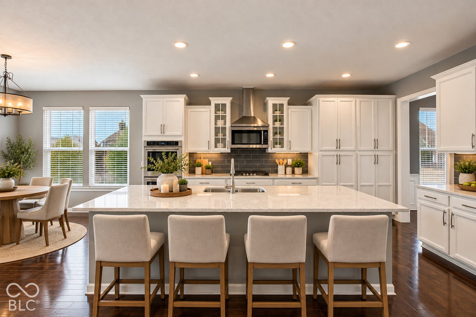 Spacious kitchen with white cabinetry, stainless steel appliances, a large center island with a light-toned countertop, and dark wood-finish flooring