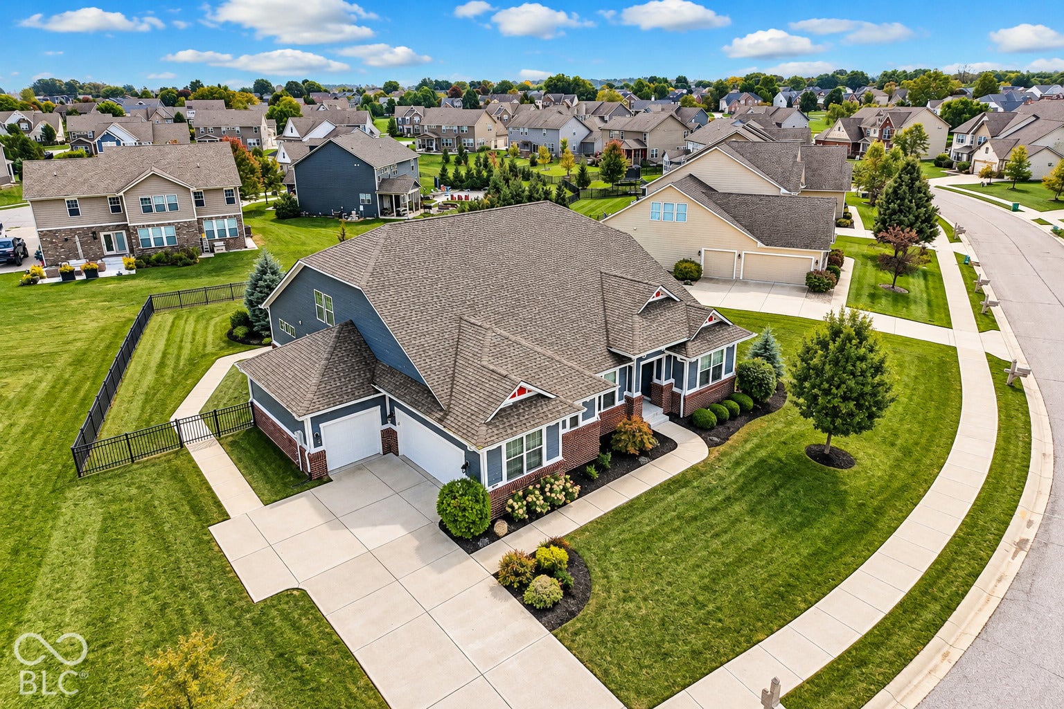 Suburban residence featuring a multi-gabled roofline, two-car garage, concrete driveway, concrete sidewalk, and a fenced yard